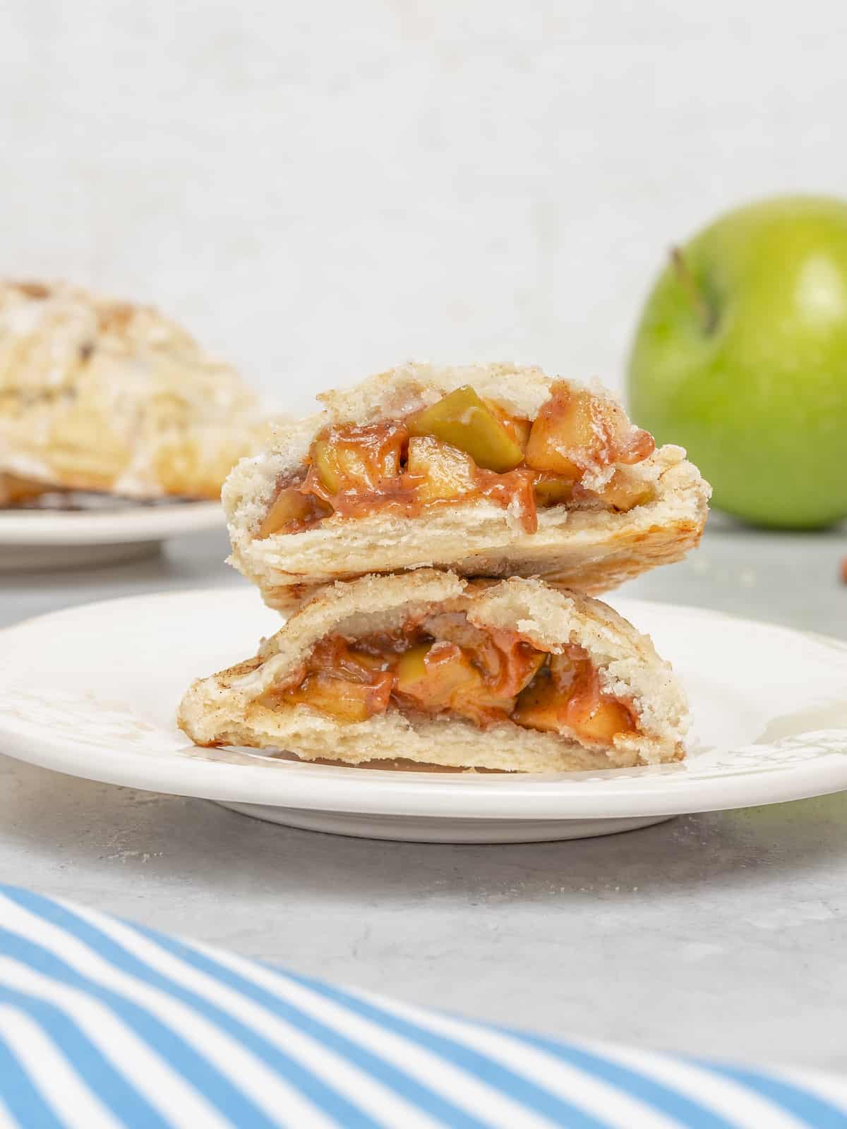 Two gluten free apple turnovers stacked on a white plate, revealing the apple filling.