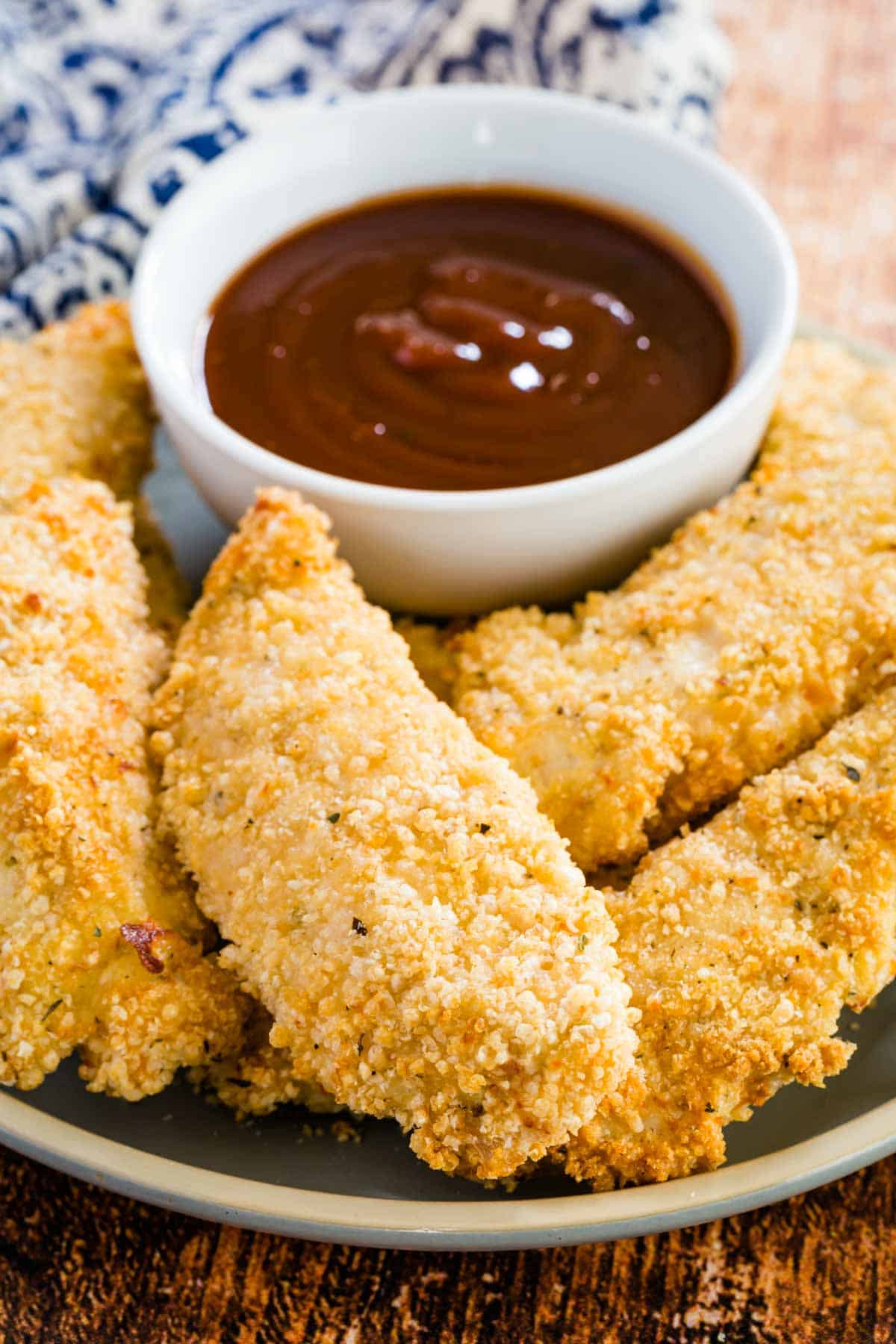 Gluten-free chicken tenders on a plate, surrounding a dish of ketchup for dipping.