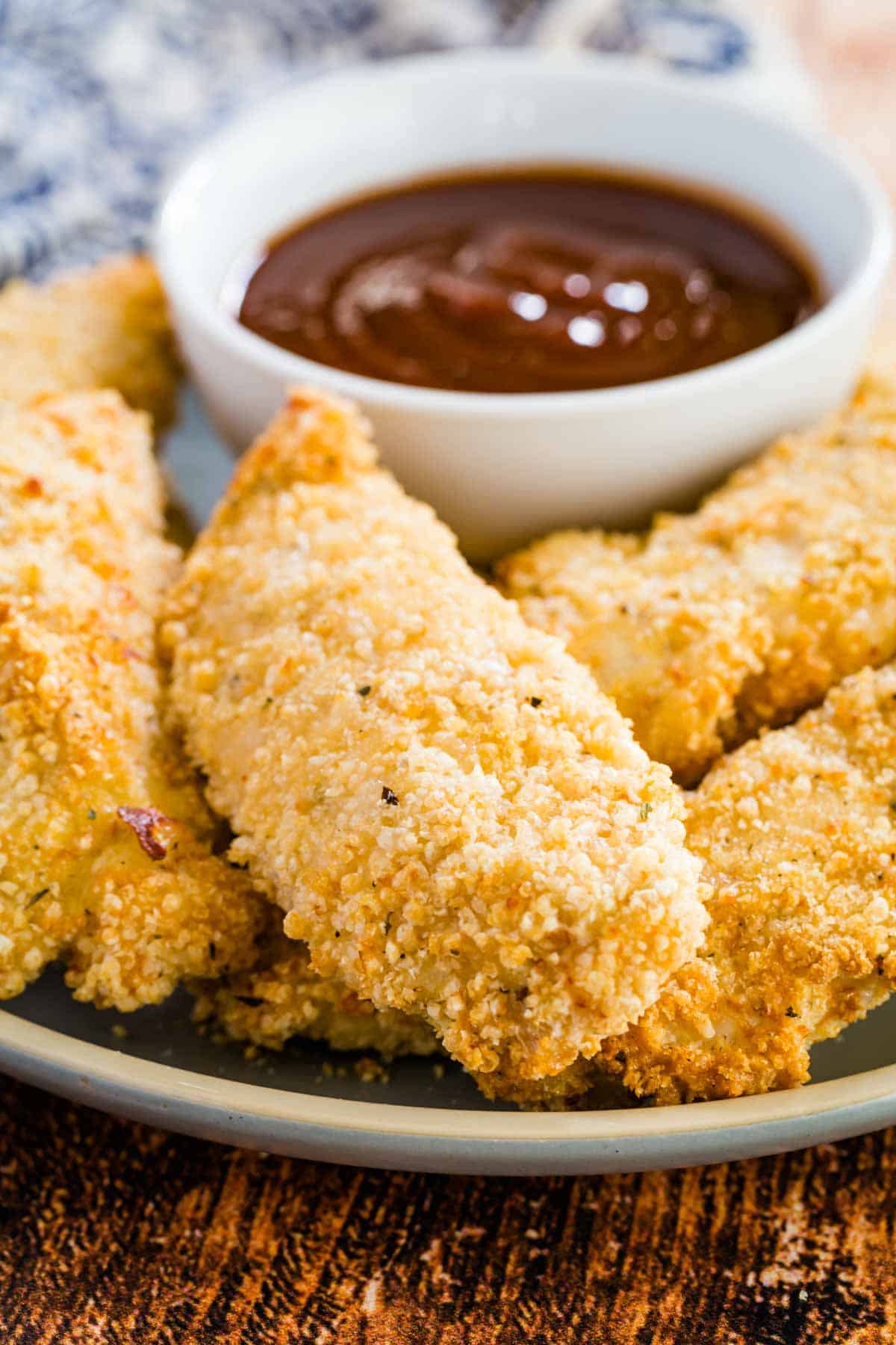 Gluten-free baked chicken tenders on a plate, surrounding a dish of ketchup for dipping.