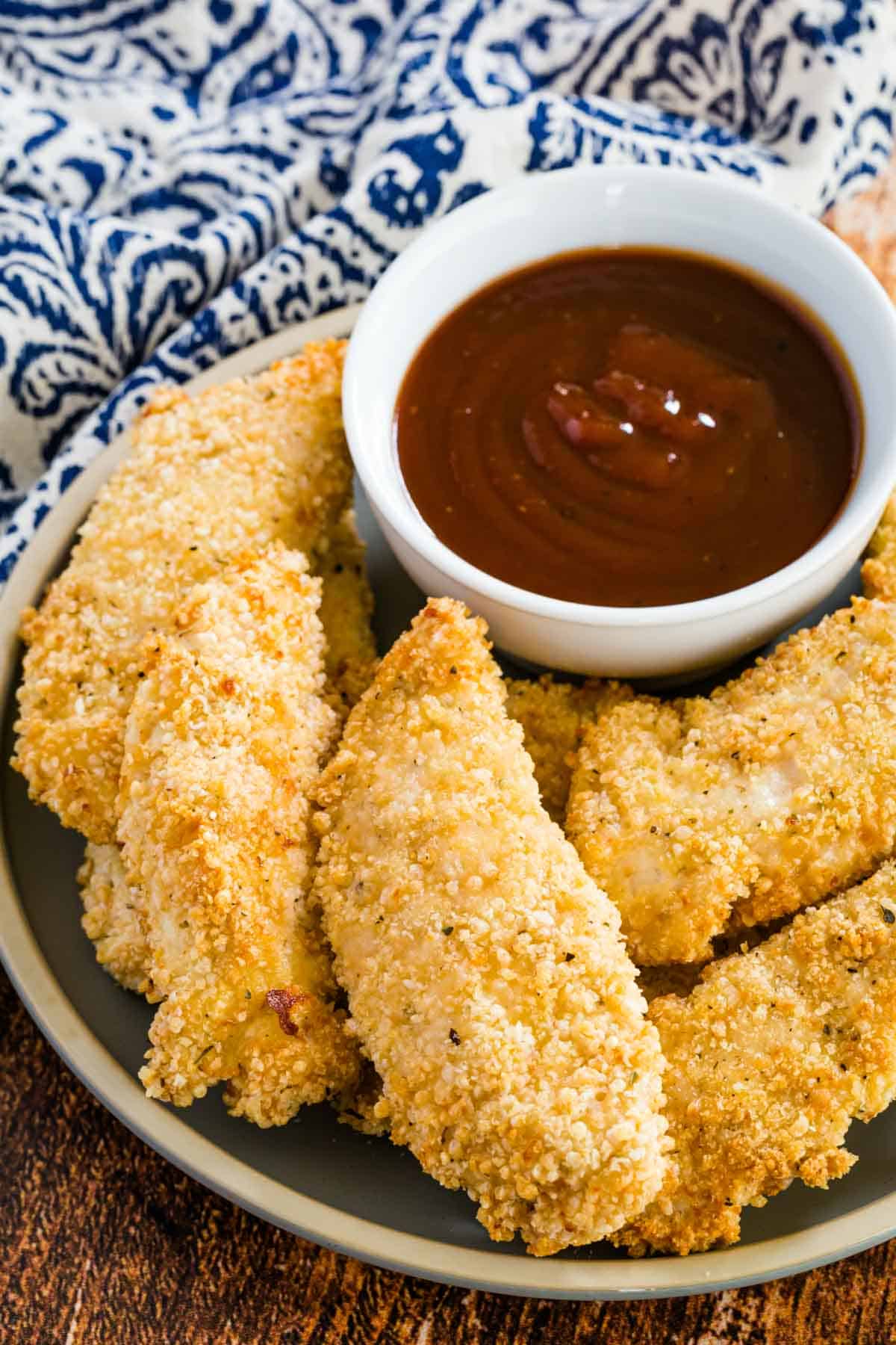 Top view of gluten-free baked chicken tenders on a plate, surrounding a dish of ketchup for dipping.
