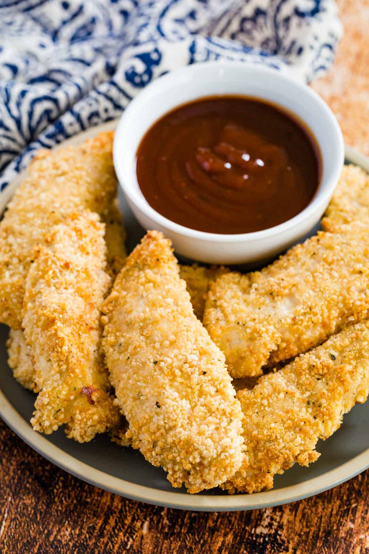 Top view of gluten-free baked chicken tenders on a plate, surrounding a dish of ketchup for dipping.