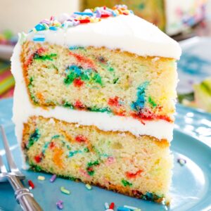 A slice of funfetti cake with sprinkles scattered on the plate.