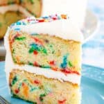 A slice of gluten free funfetti cake with two layers and vanilla frosting on a blue plate.