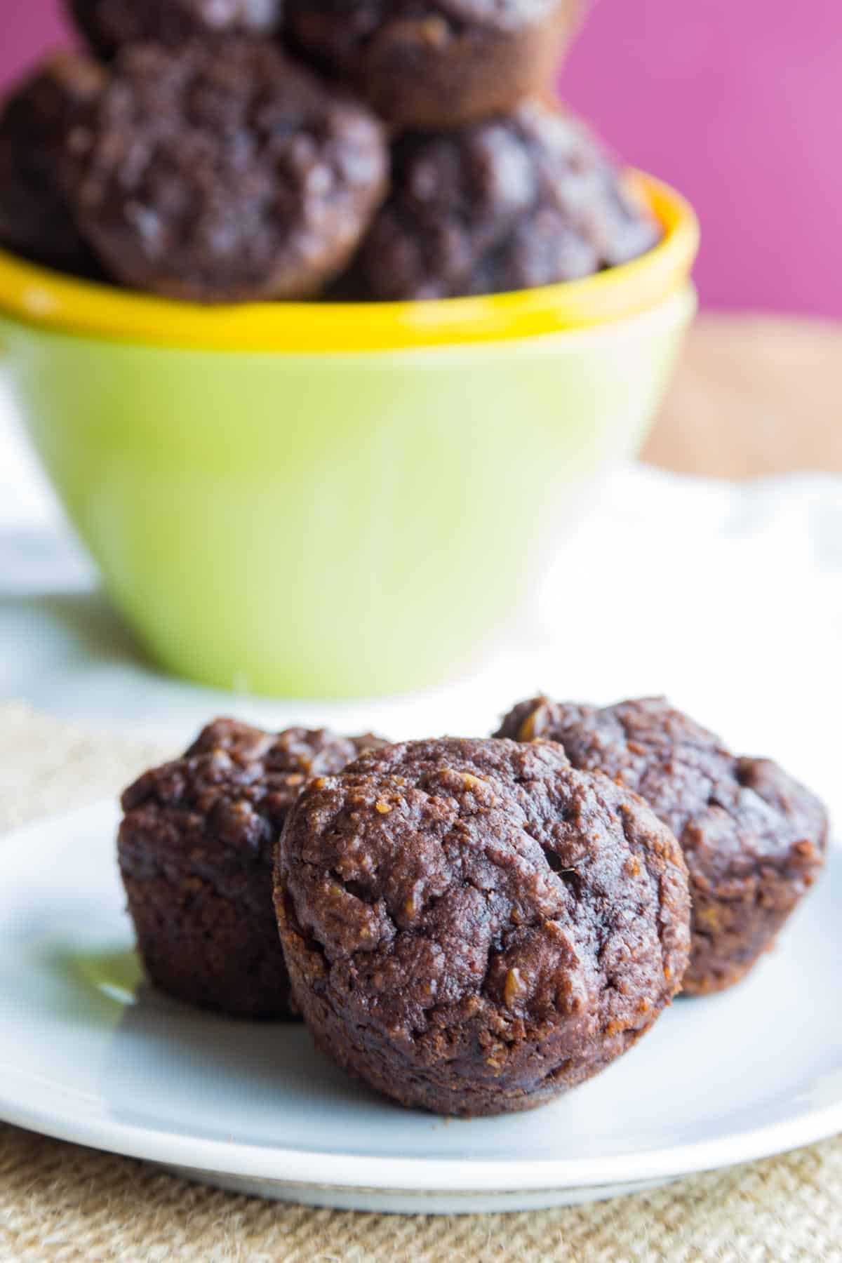 A plate with three Flourless Nutella Pumpkin Muffins in front of a bowl with the rest of the batch.