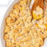 A wooden spoon in a baking dish of peach cobbler.