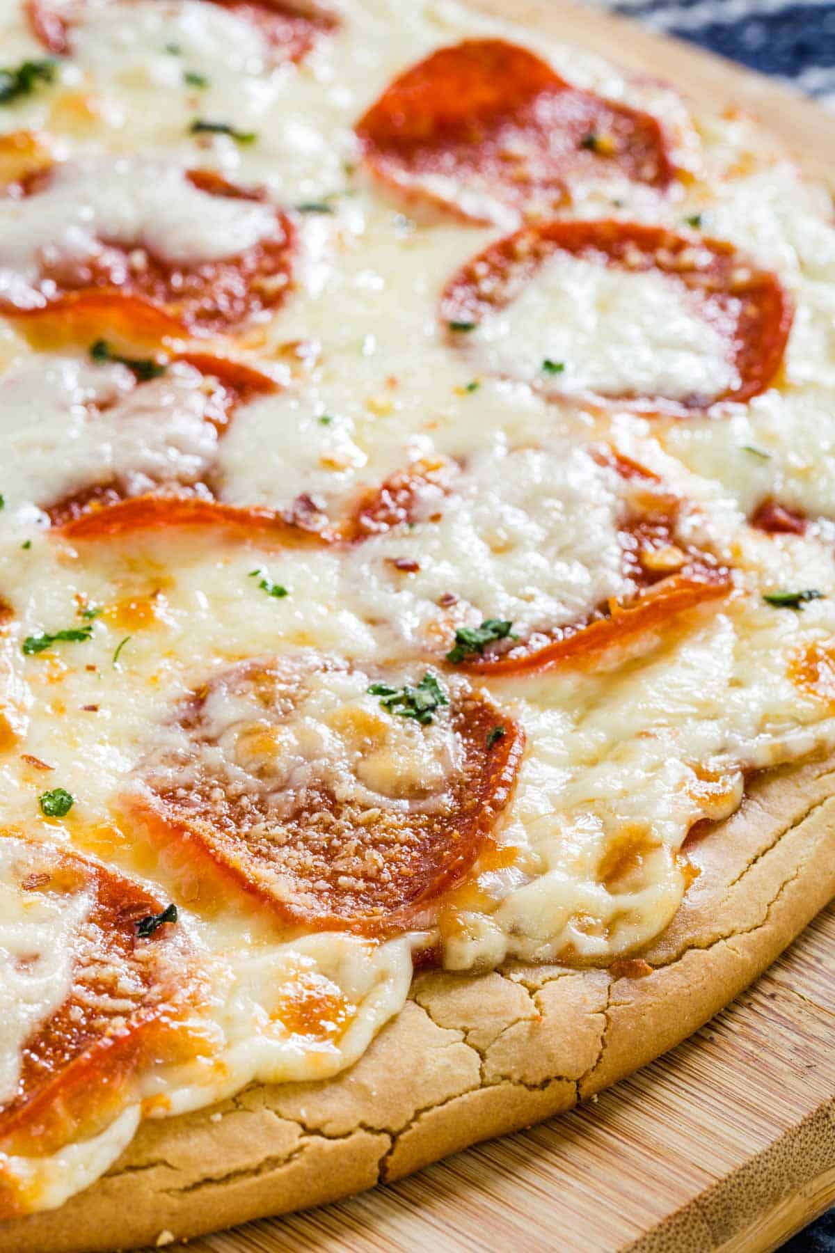 Close up of a whole gluten free pepperoni pizza on a wooden cutting board.