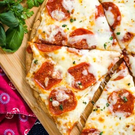 Top view of a gluten free pepperoni pizza cut into slices on a wooden cutting board.