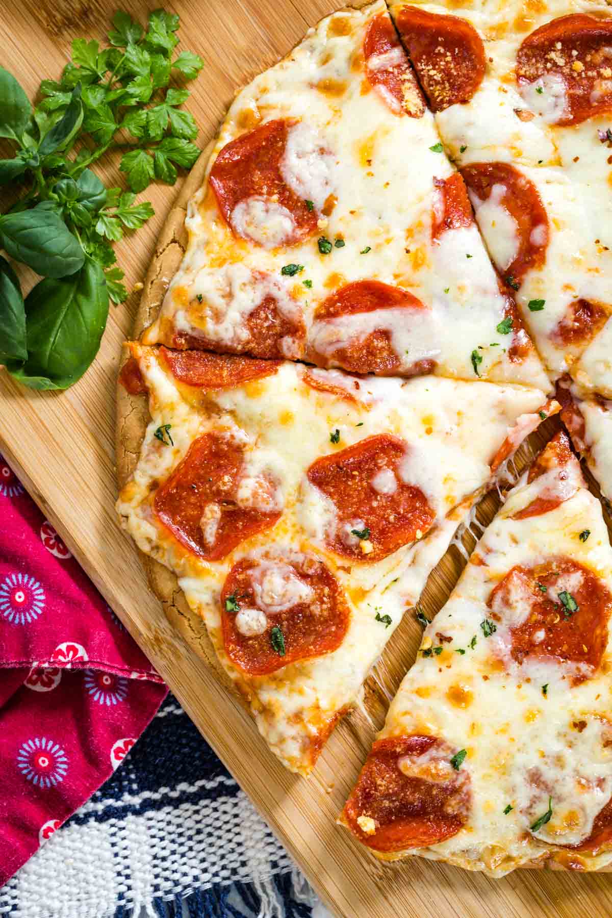 Top view of a gluten free pepperoni pizza cut into slices on a wooden cutting board.