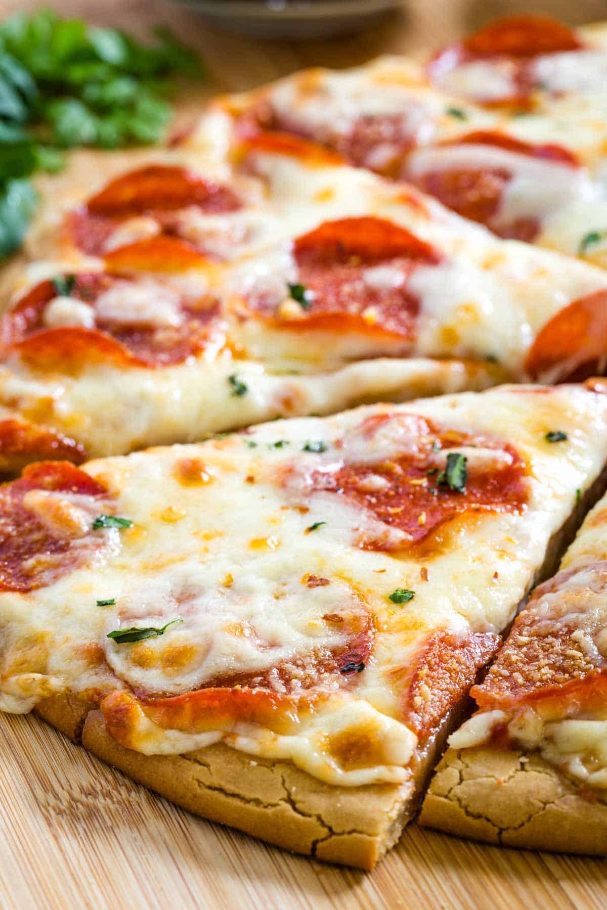 Gluten free pepperoni pizza cut into slices on a wooden cutting board.