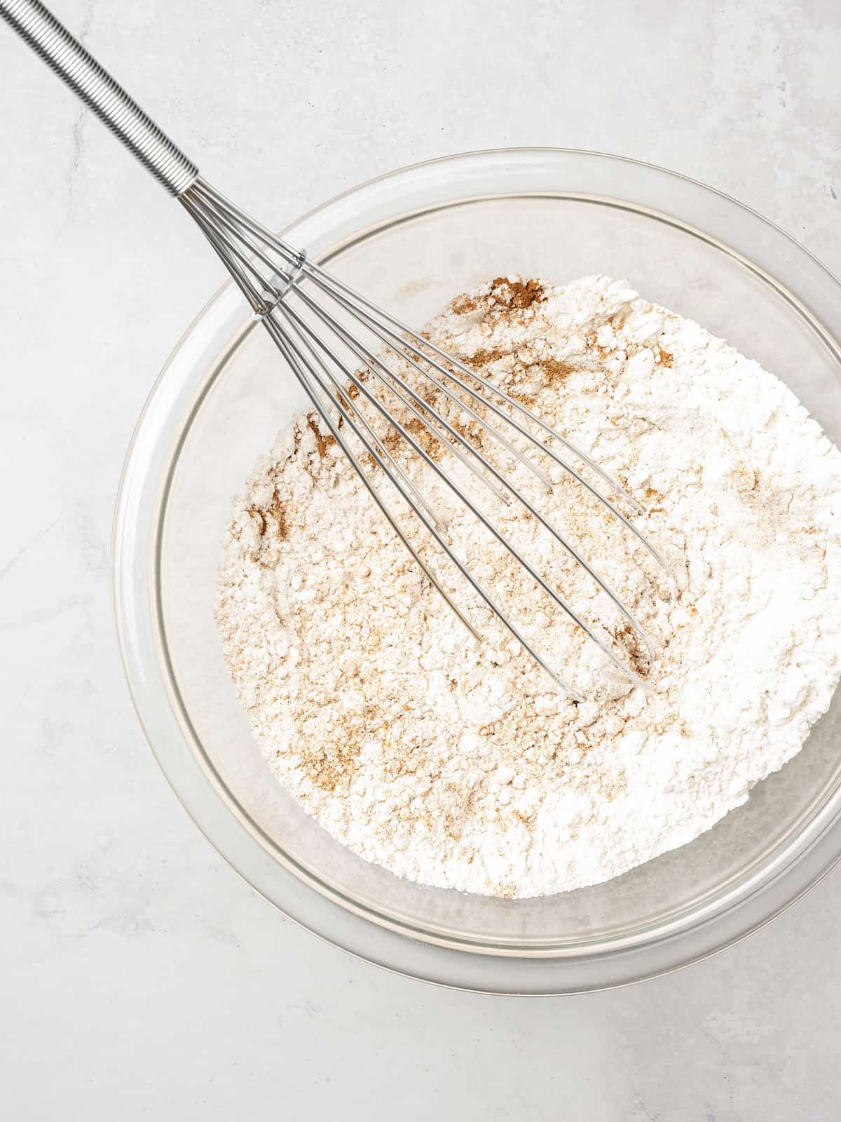 The dry ingredients for gluten free pumpkin cupcakes are whisked together in a glass bowl.