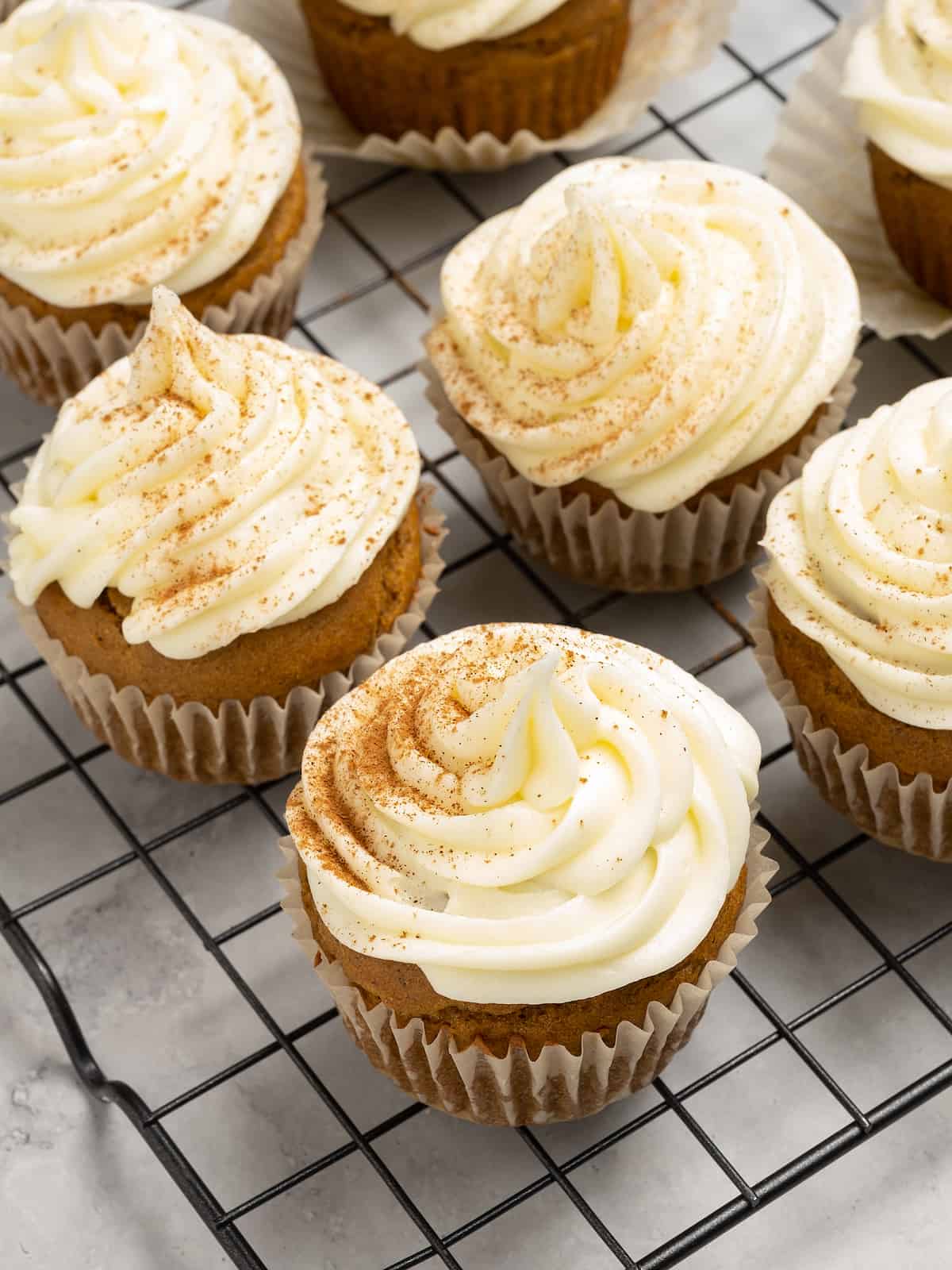 Frosted gluten free pumpkin cupcakes sprinkled with cinnamon on a wire rack.