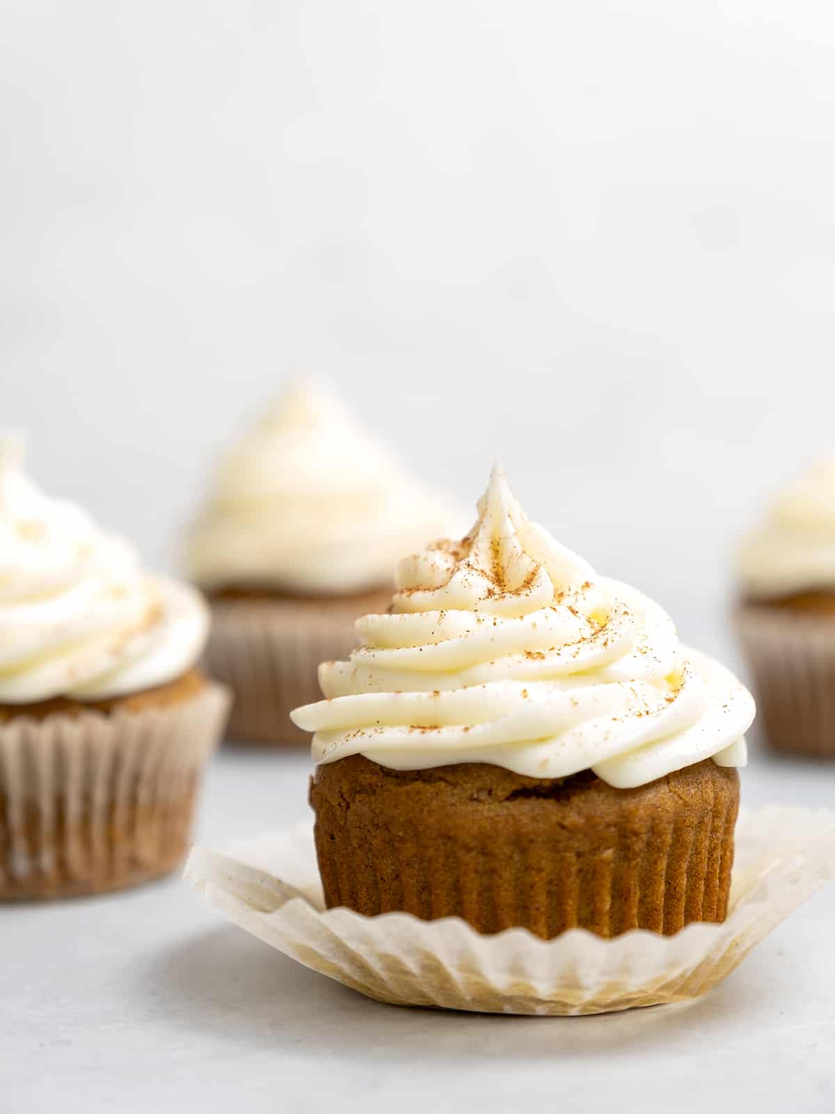 Side view of gluten free pumpkin cupcakes topped with swirls of cream cheese frosting.