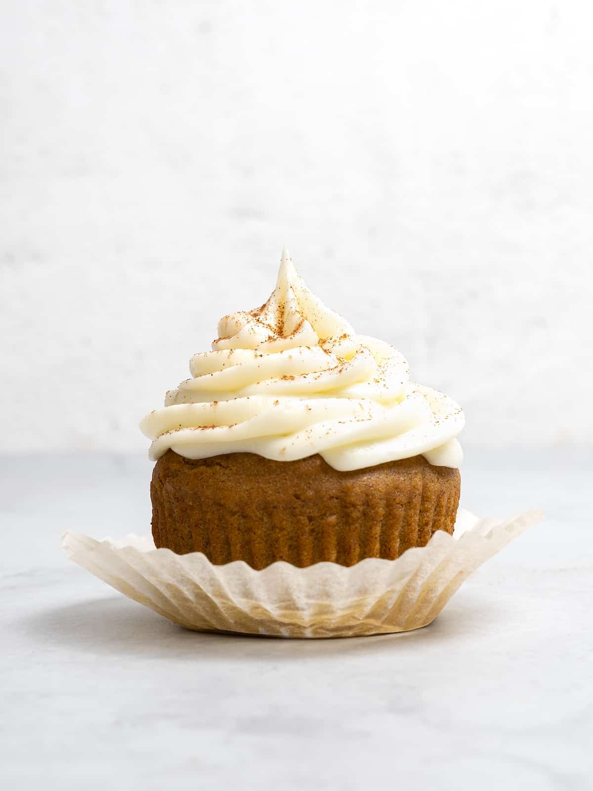 Side view of a gluten free pumpkin cupcake topped with swirls of cream cheese frosting.