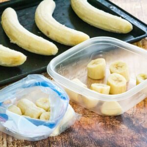 Frozen banana chunks in a plastic bag and a storage container and whole ones on a baking sheet.