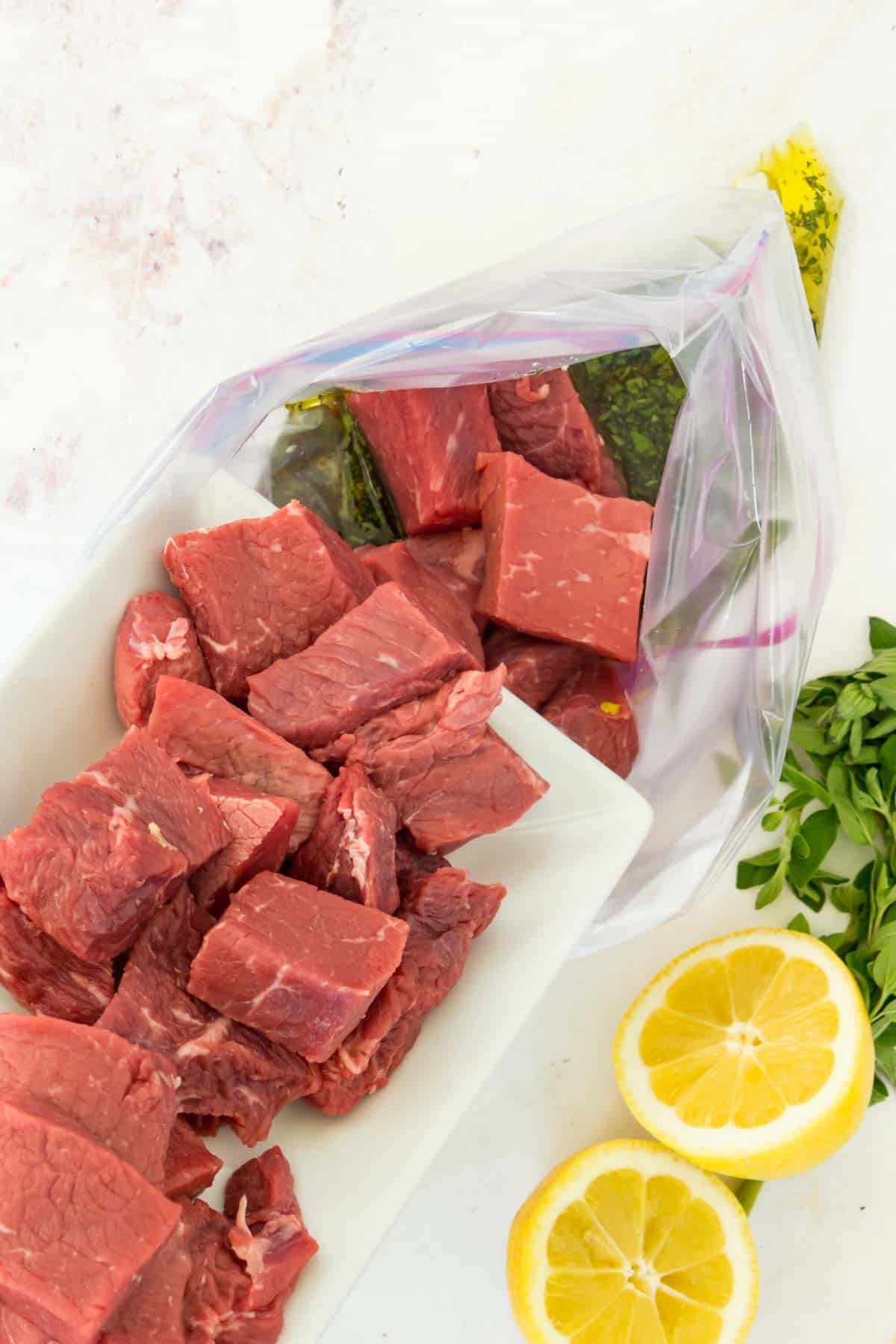 Adding the raw cubes of beef to a plastic ziptop bag with the souvlaki marinade.