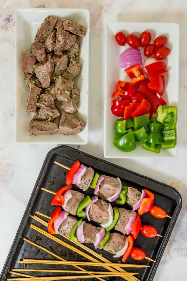 Marinated beef and vegetables on plates and some threaded onto bamboo skewers.