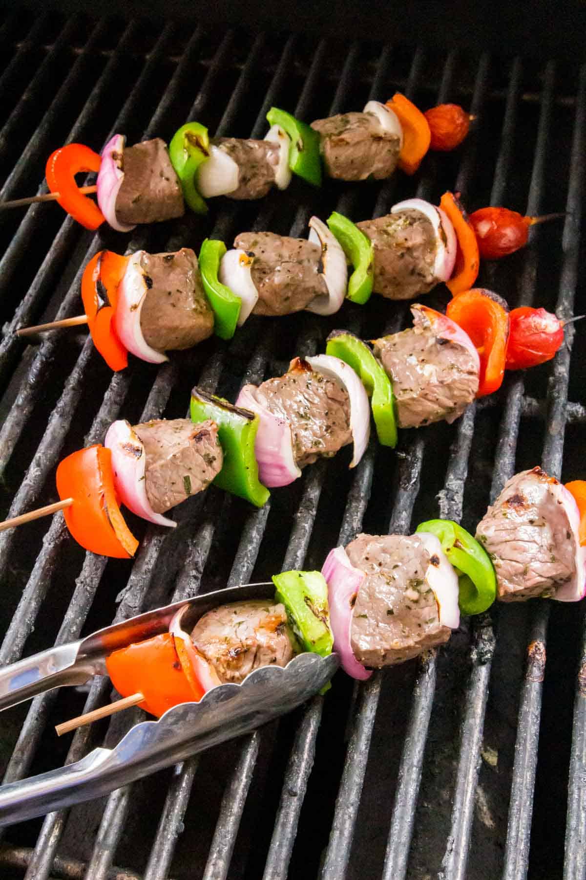 beef kabobs being flipped on the grill with tongs.