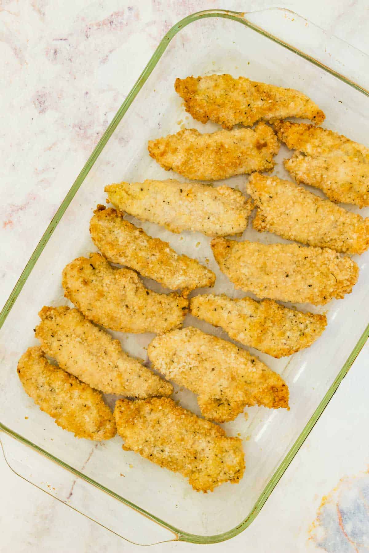 Rows of crispy chicken tenders in a glass baking dish.