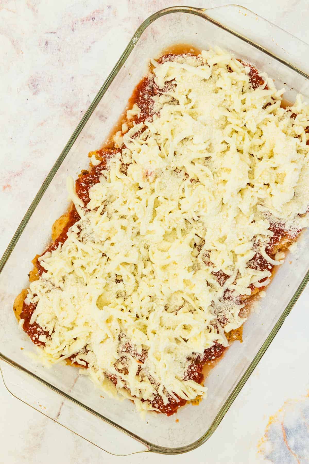 Top view of assembled chicken parmesan in a glass baking dish, ready to be baked.