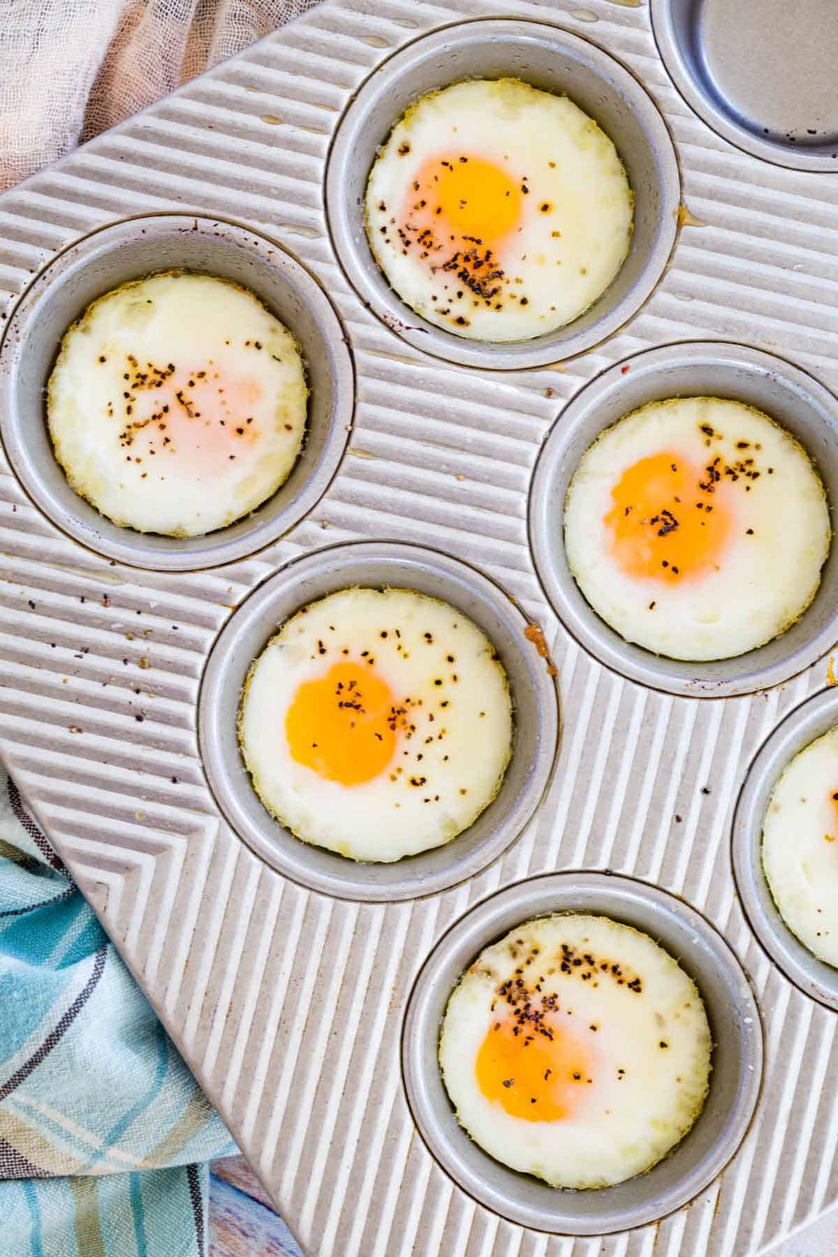 Top view of seasoned baked eggs in the wells of a metal muffin pan.