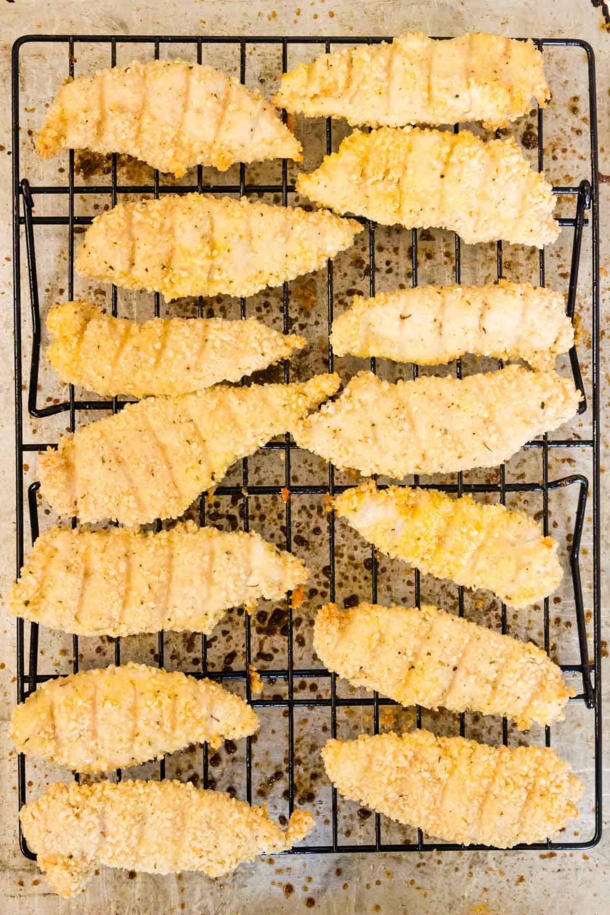 Top view of baked chicken tenders in rows on a wire rack on top of a baking sheet.