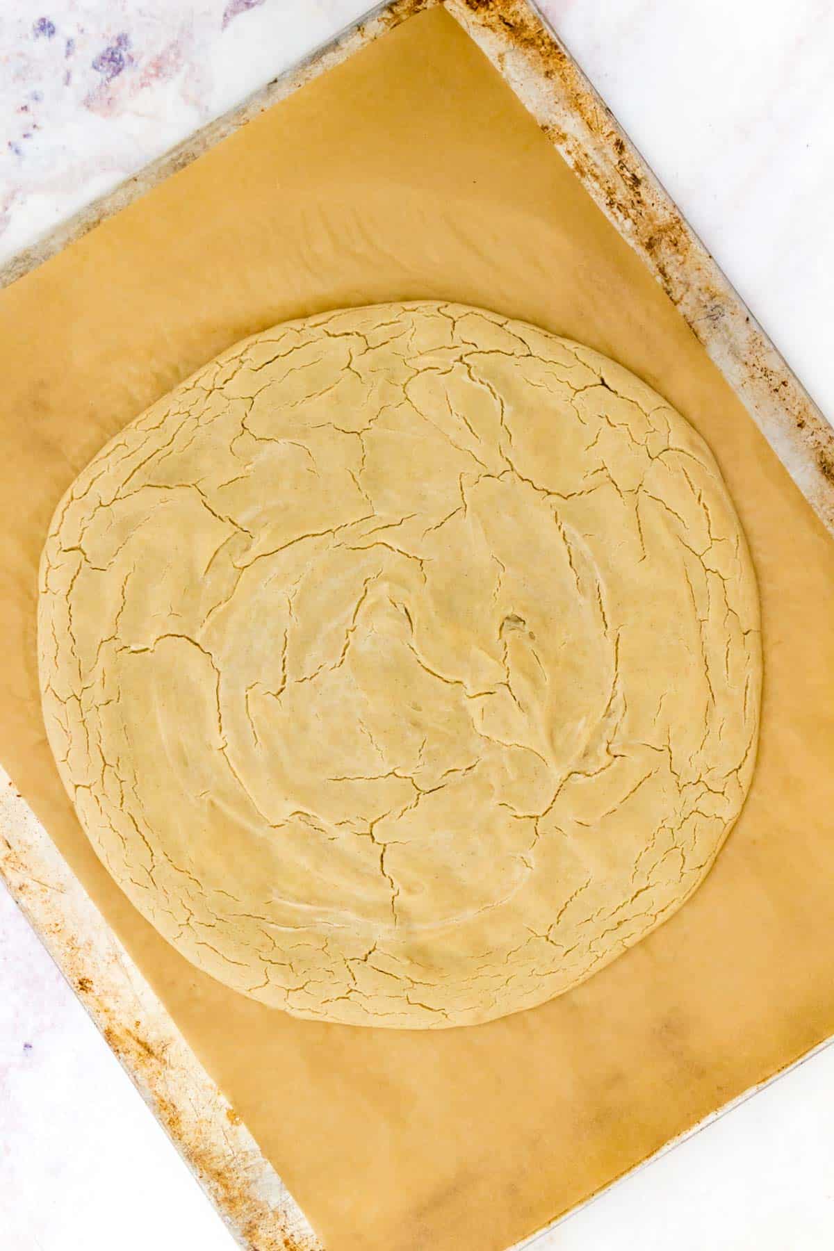 Par-baked gluten free pizza crust on a parchment-lined baking sheet.