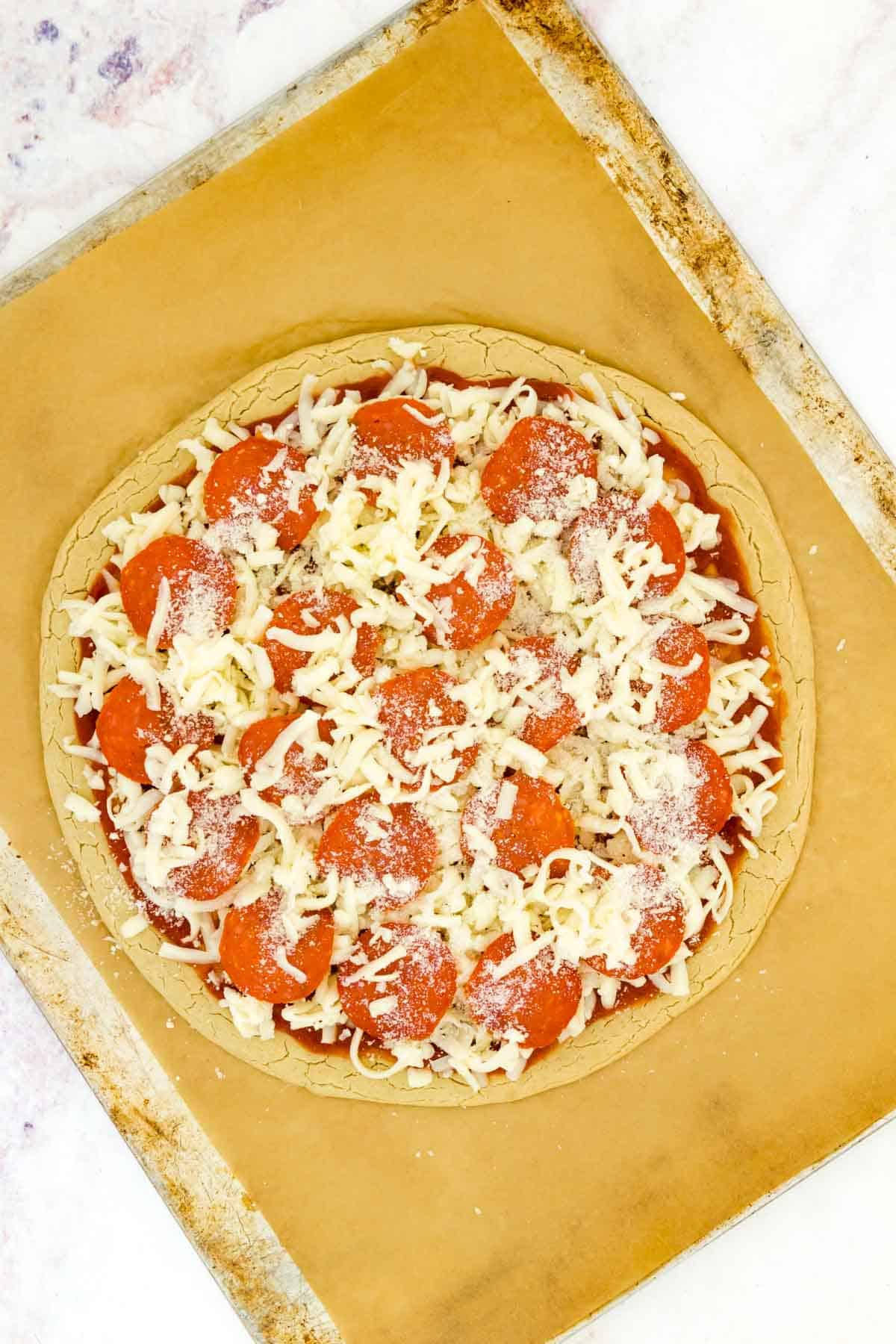 Unbaked gluten free pepperoni pizza on a parchment-lined baking sheet.