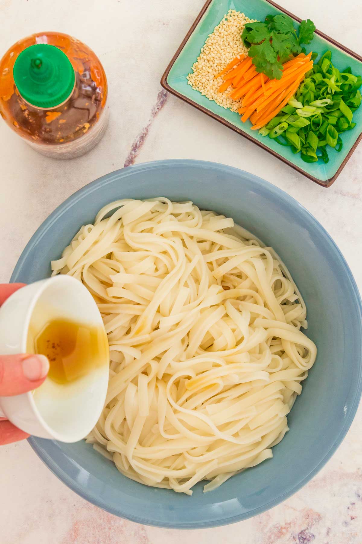 Sesame oil being added to a bowl of cooked pasta.