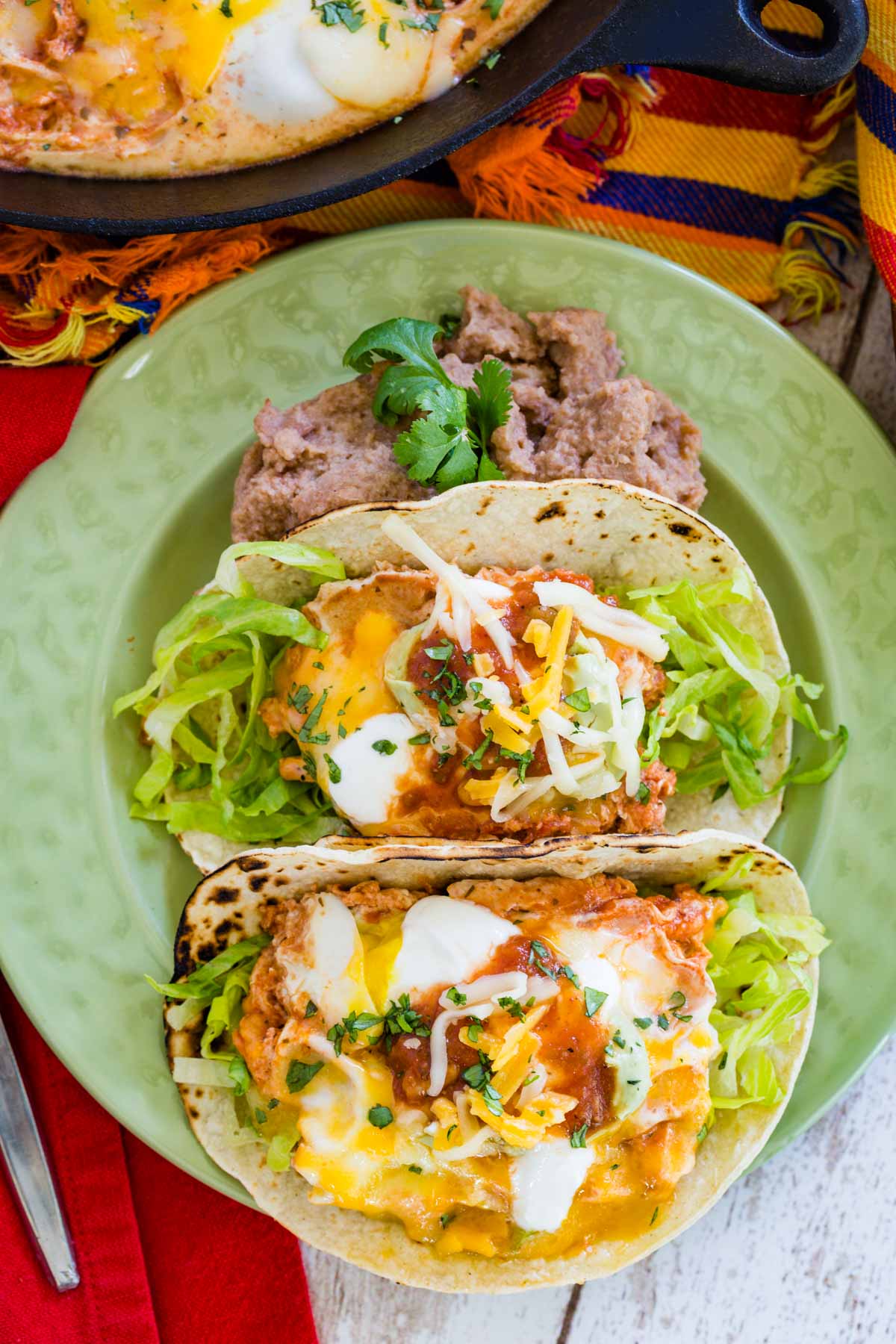 Two Salsa Egg Tacos with lettuce and shredded cheese next to a dollop of refried beans.