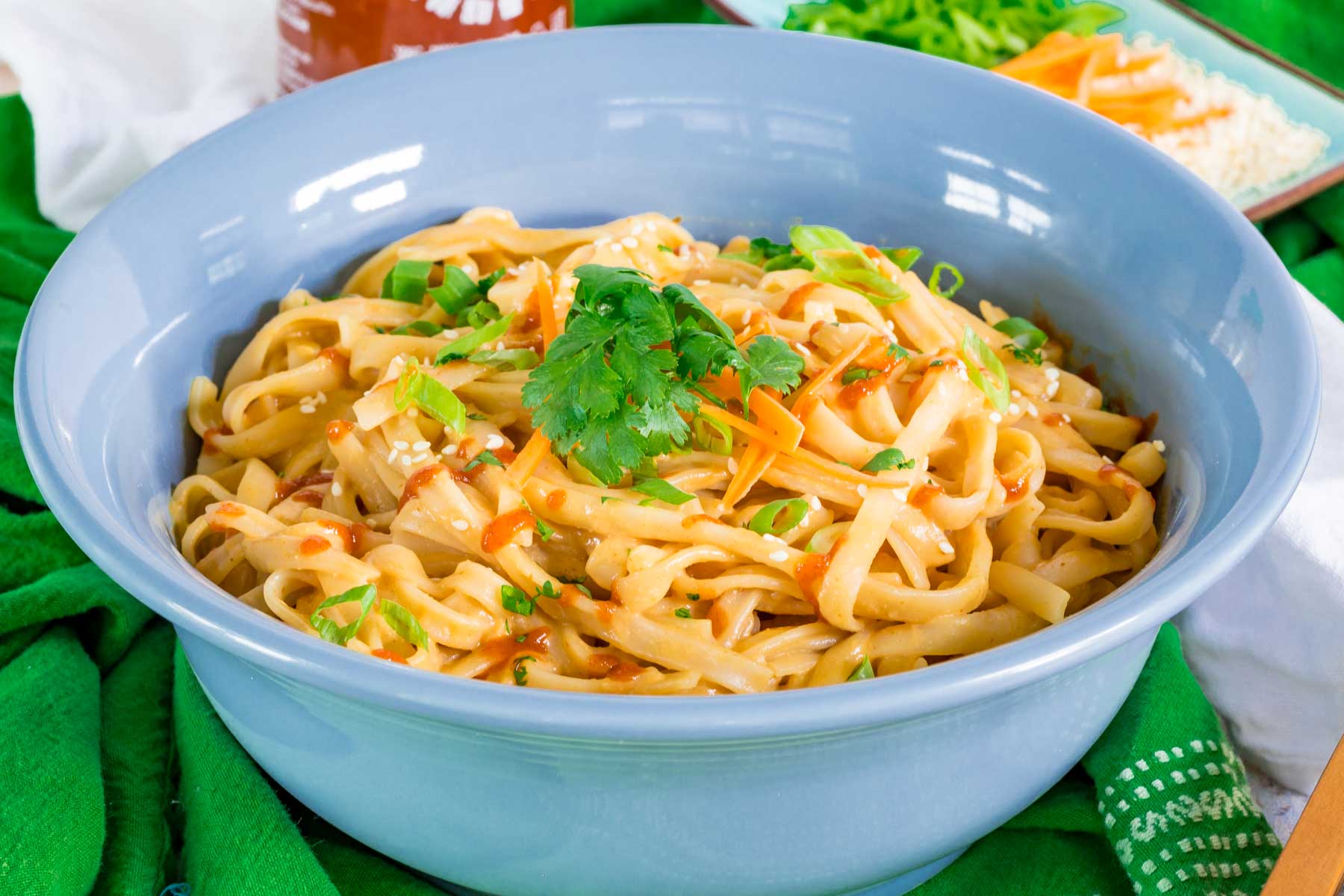 Spicy Sesame Noodles in a bowl with chopped and shredded vegetables as garnish.