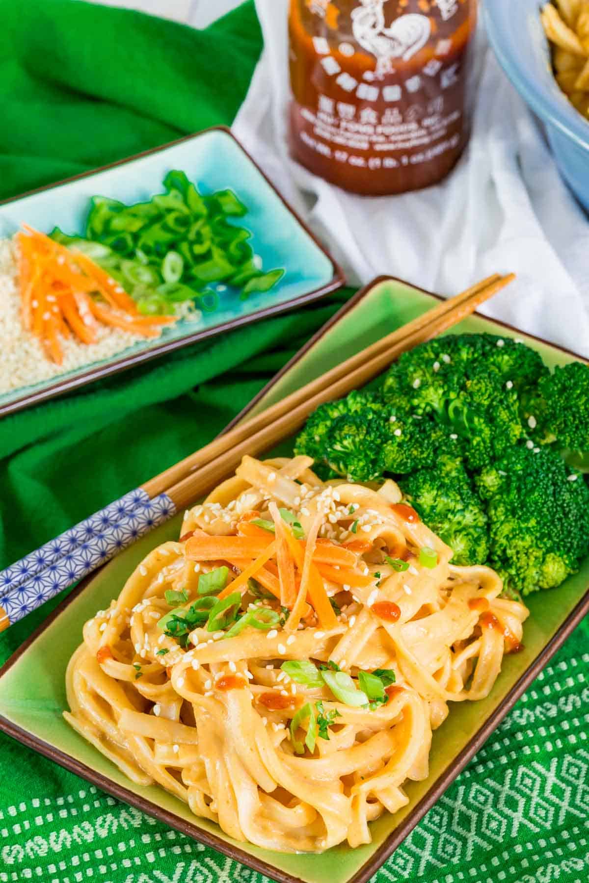 A place of sesame noodles with broccoli alongside a small plate of garnishes for the noodles.