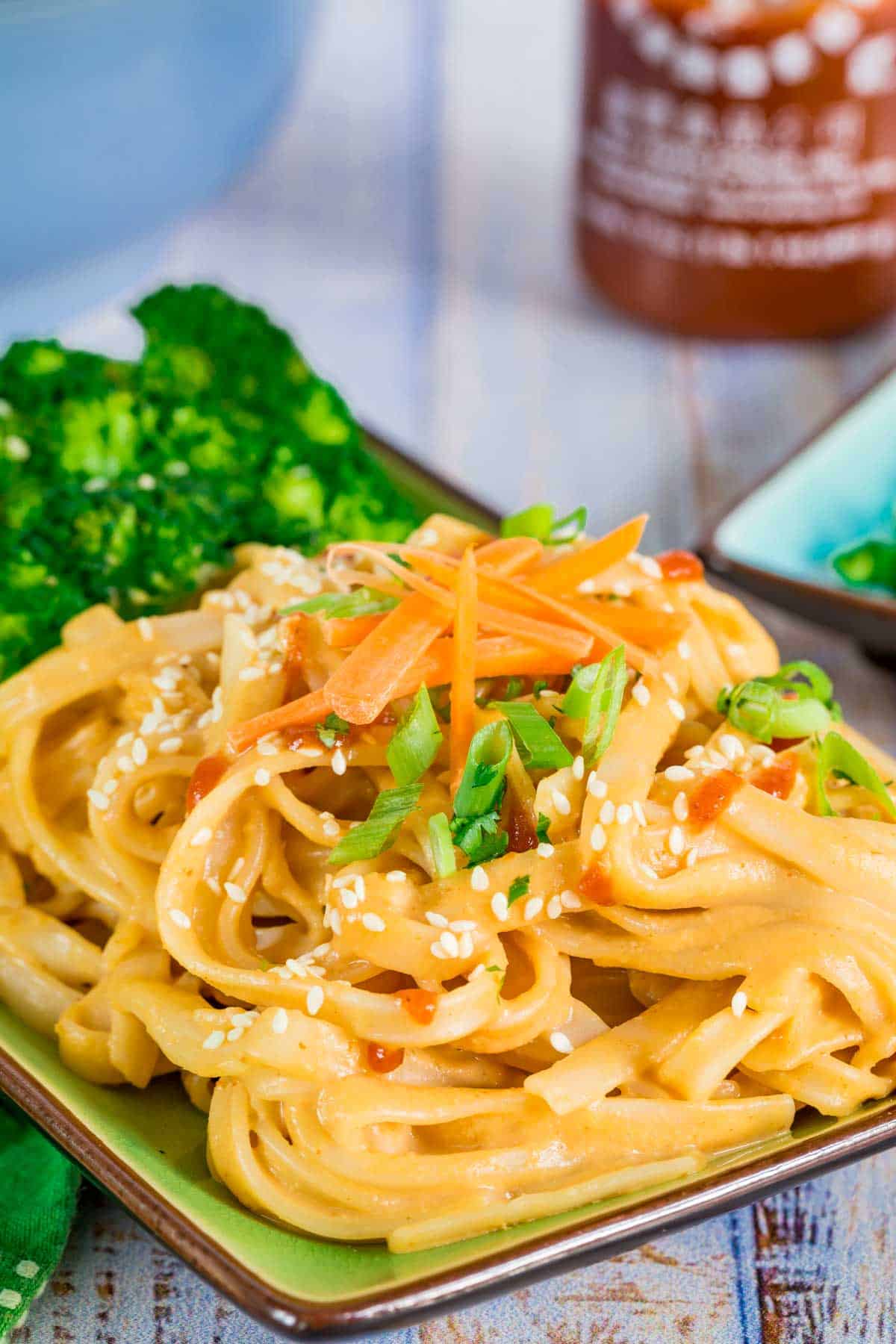 A serving of sesame noodles with broccoli on a rectangular plate garnished with sesame seeds and scallions.