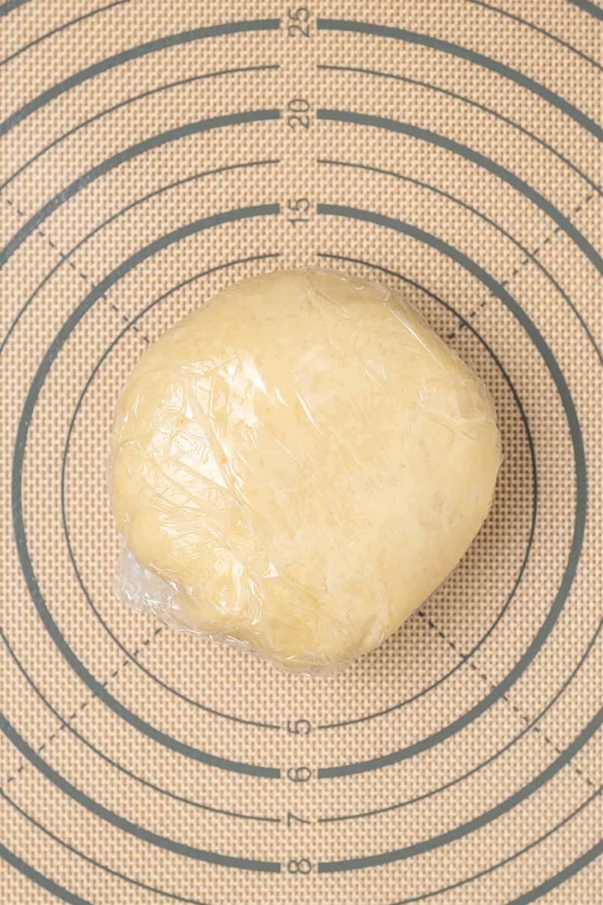 A ball of gluten free pizza dough wrapped in plastic wrap.