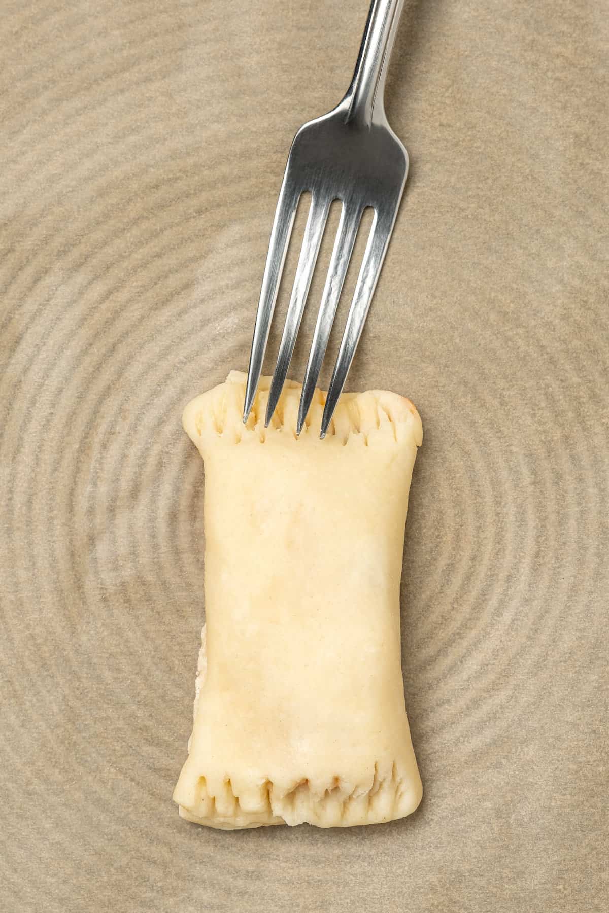 A fork is used to crimp the dough edges of a folded pizza roll.