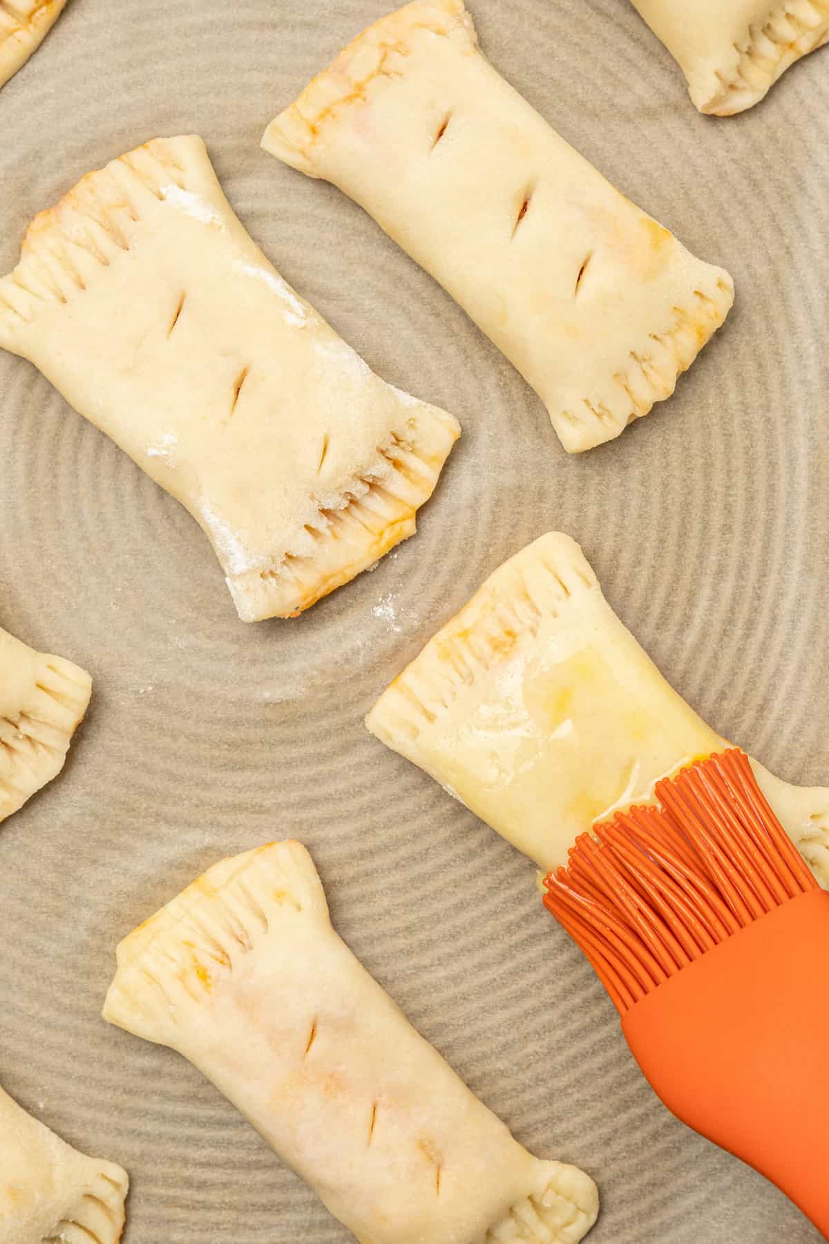 Overhead view of unbaked gluten free pizza rolls are brushed with egg wash.