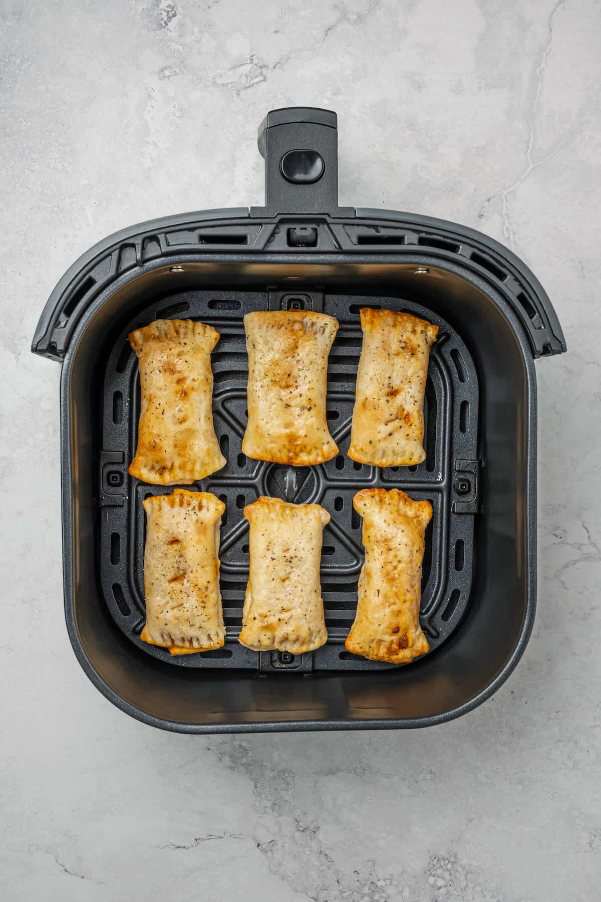 Overhead view of crispy gluten free pizza rolls inside the air fryer.