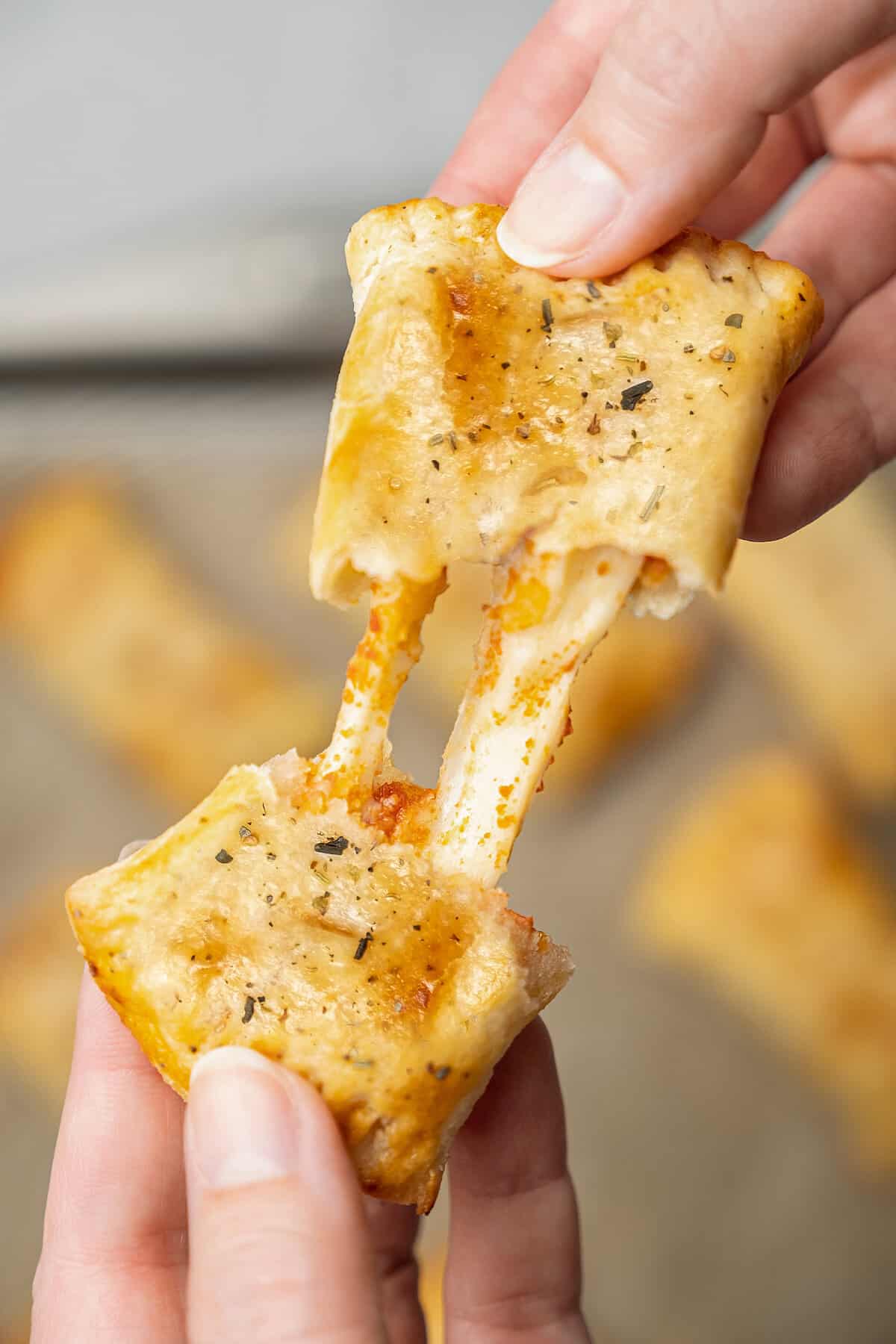 Two hands pull apart an air fryer pizza roll to reveal the melted cheese filling.