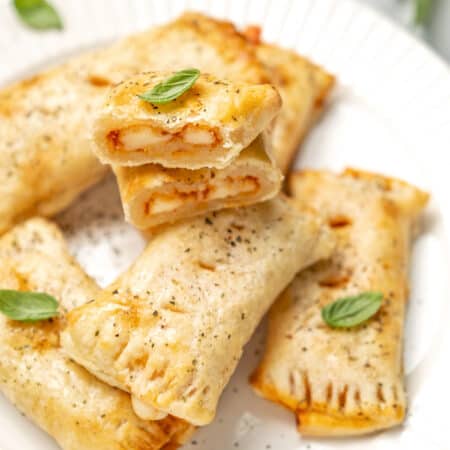 Air fryer gluten free pizza rolls on a white plate, garnished with basil leaves.