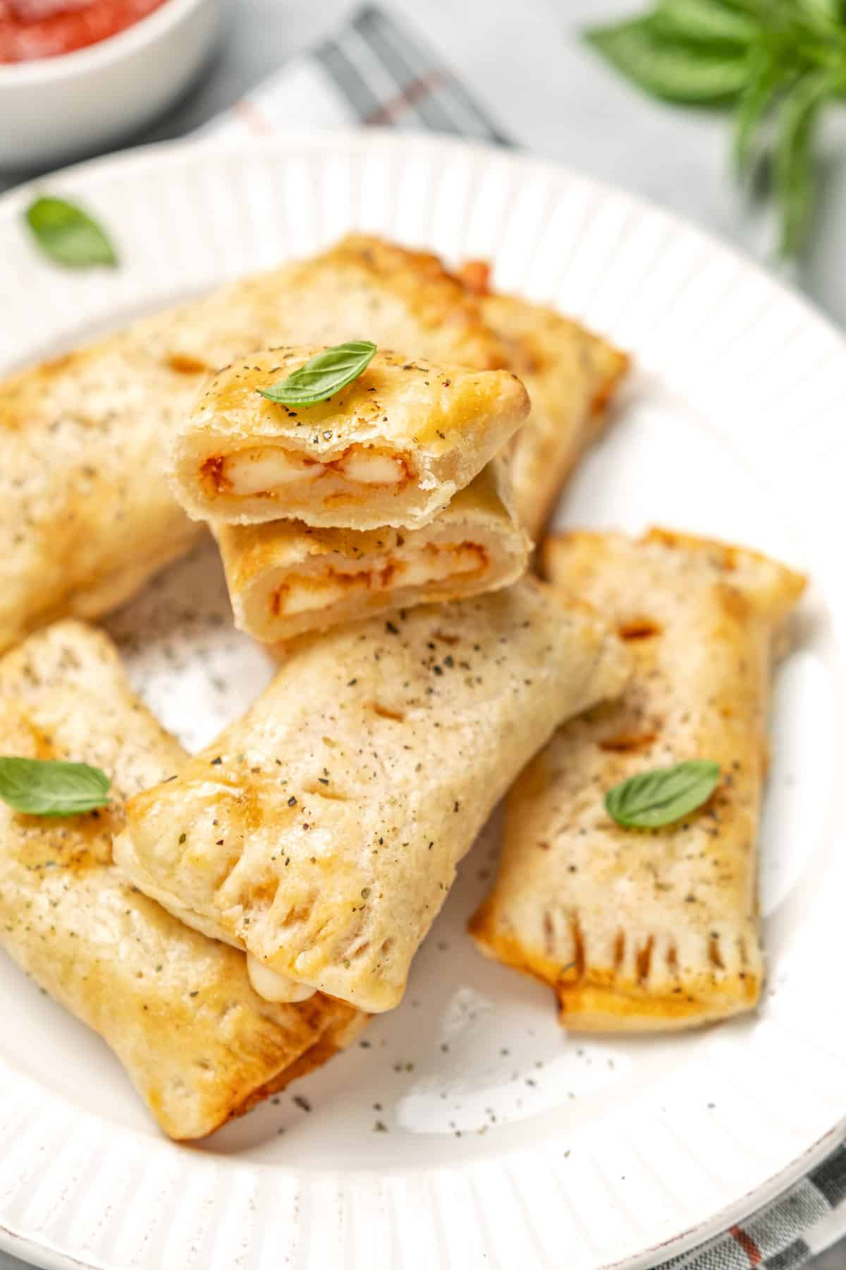 Air fryer gluten free pizza rolls on a white plate, garnished with basil leaves.