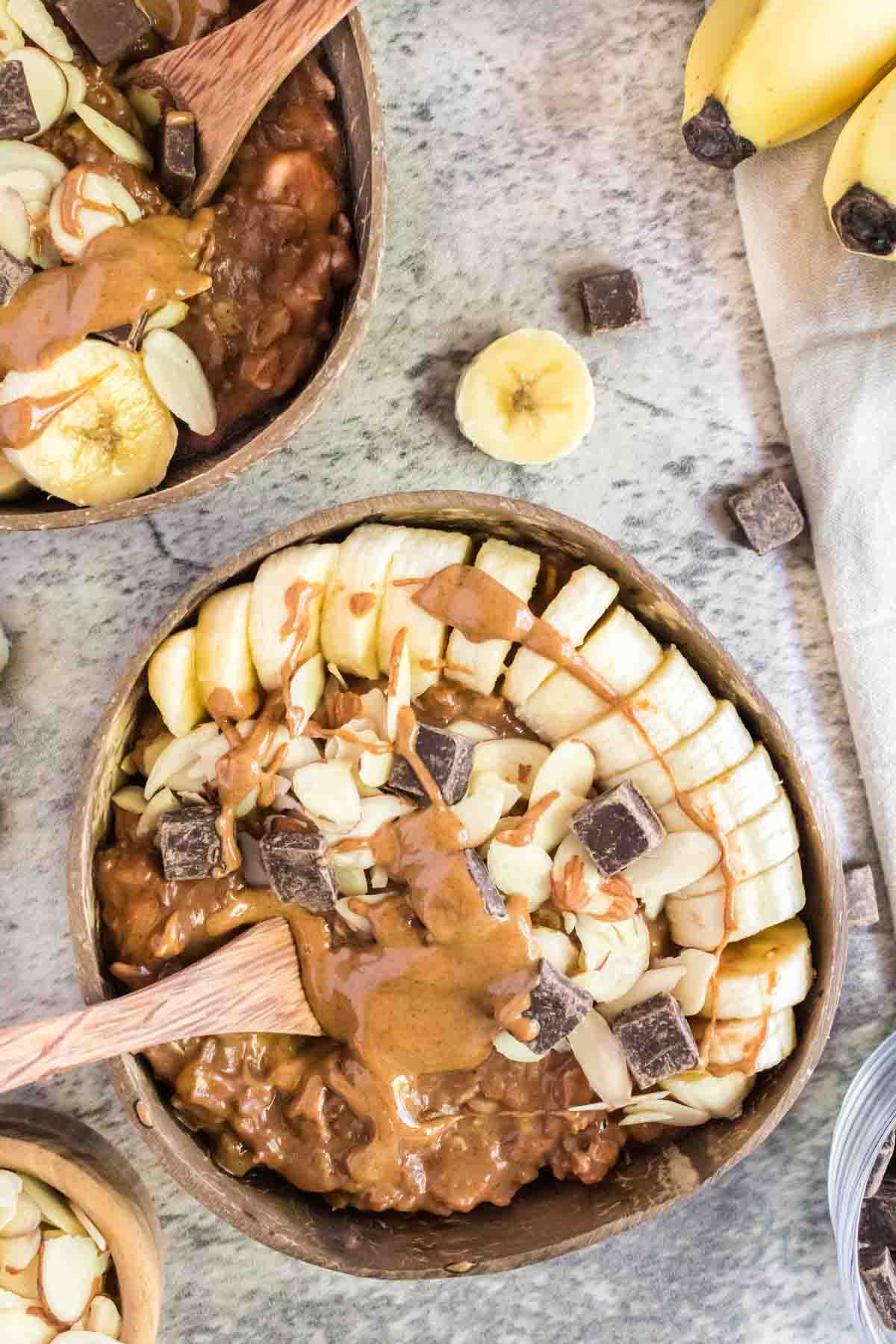 A bowl of Almond Butter Chocolate Oatmeal with banana slices, chopped almonds, chocolate chunks and melted almond butter.