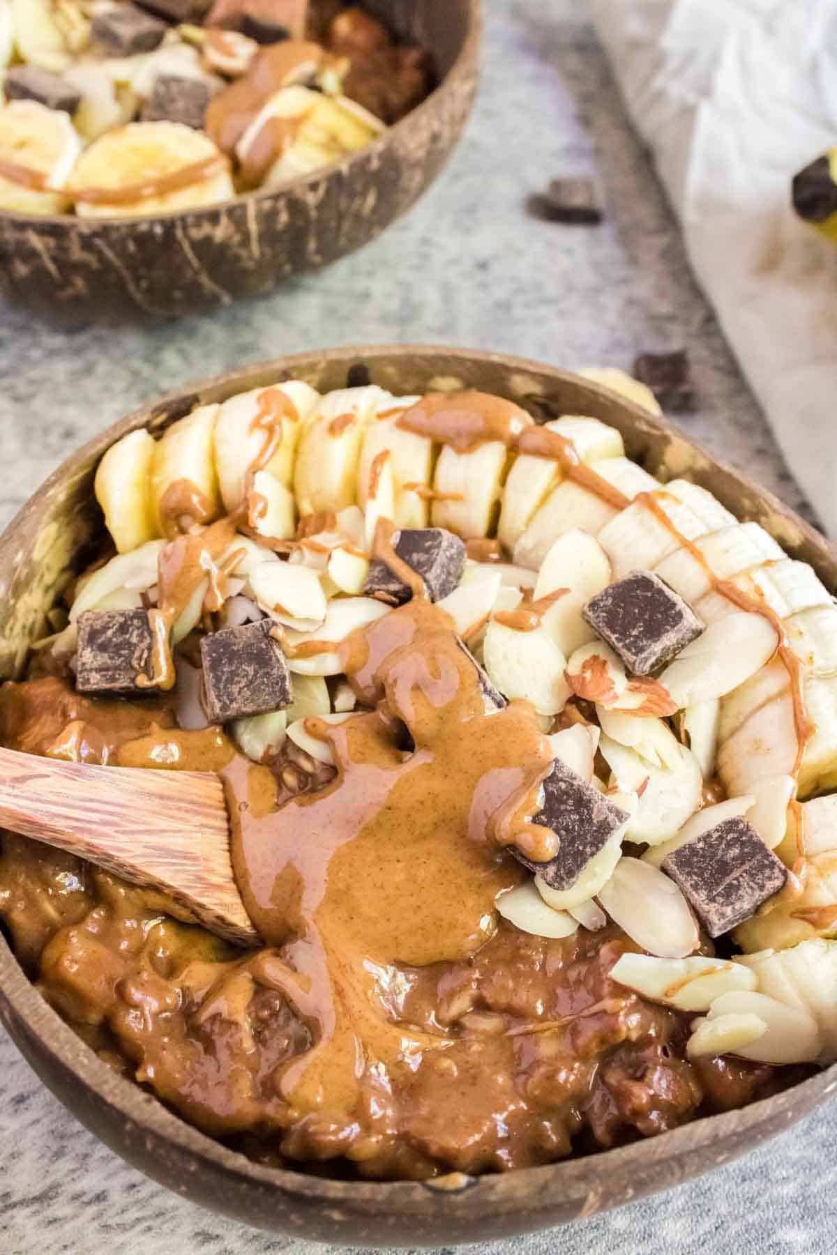 A bowl of chocolate oatmeal topped with a drizzle of almond butter, sliced almonds, chocolate chunks, and banana slices.