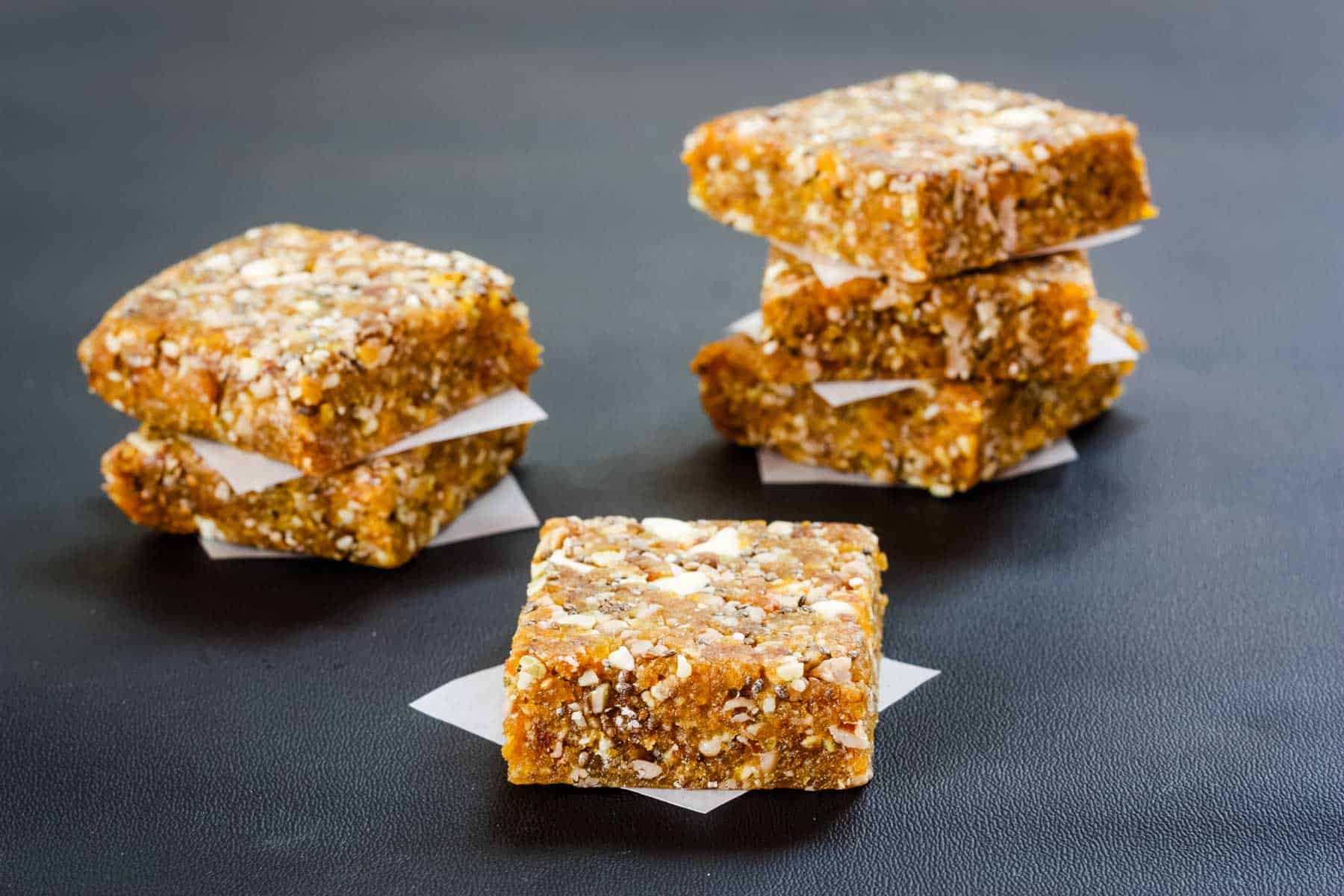 An apricot energy bar on a piece of wax paper with two stacks of energy bars behind it.