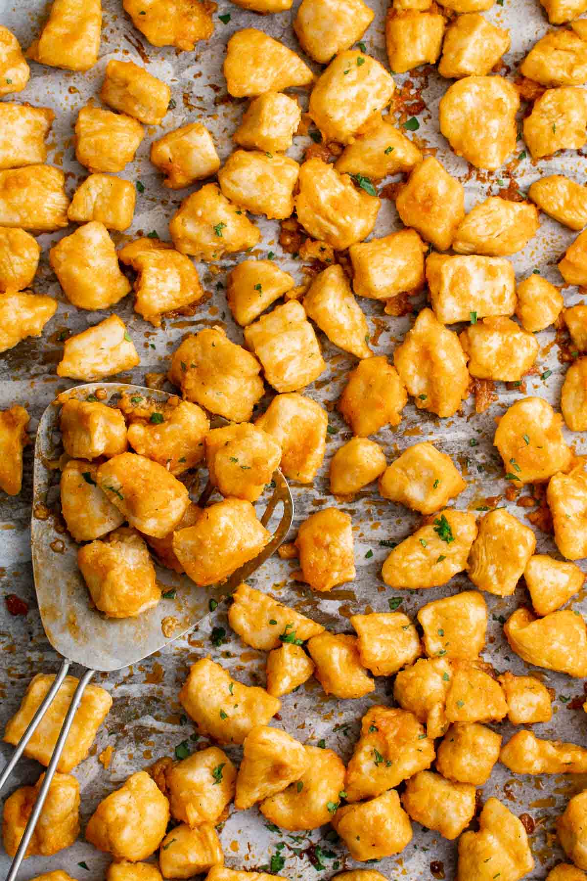 Baked buffalo chicken bites on a baking sheet with a metal serving utensil.