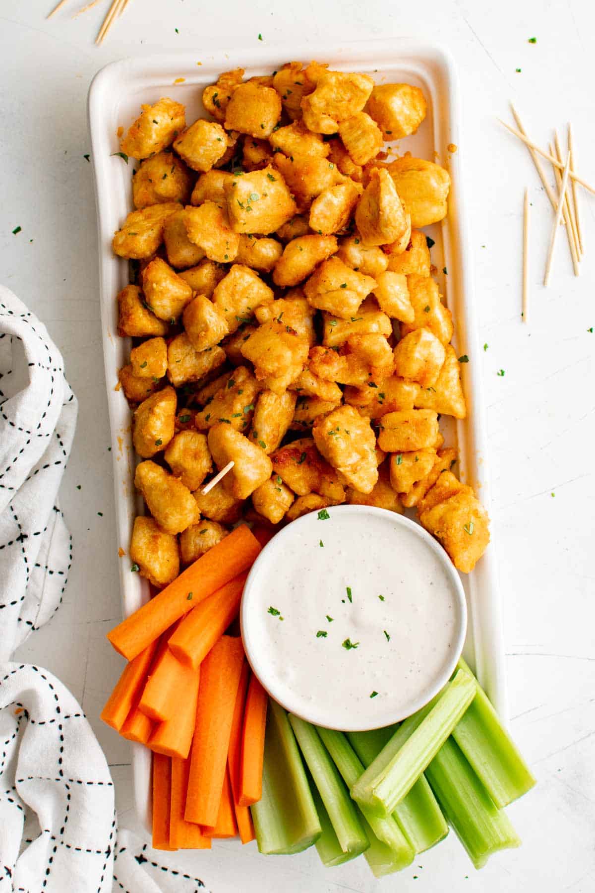 Top view of a full platter of buffalo chicken bites with a bowl of white dipping sauce and crudités.