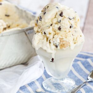 Cookie dough ice cream in a glass dish melting a little over the sides and onto a blue and white striped napkin.