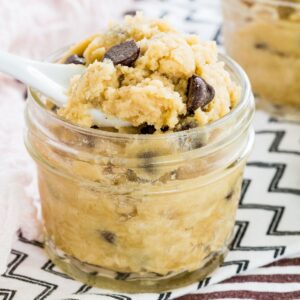 A small jar of edible cookie dough with a small white spoon in it.