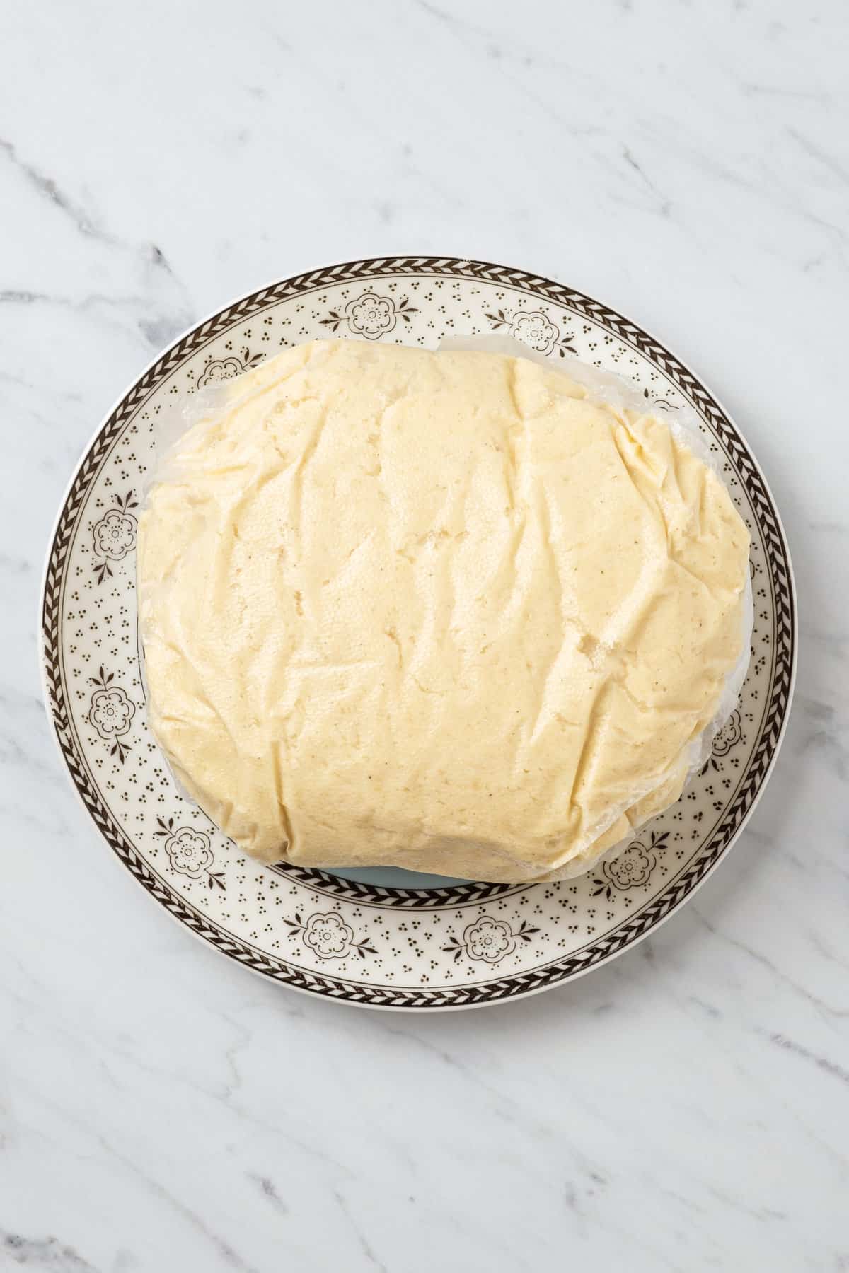 A ball of crescent roll dough wrapped in plastic on a plate.