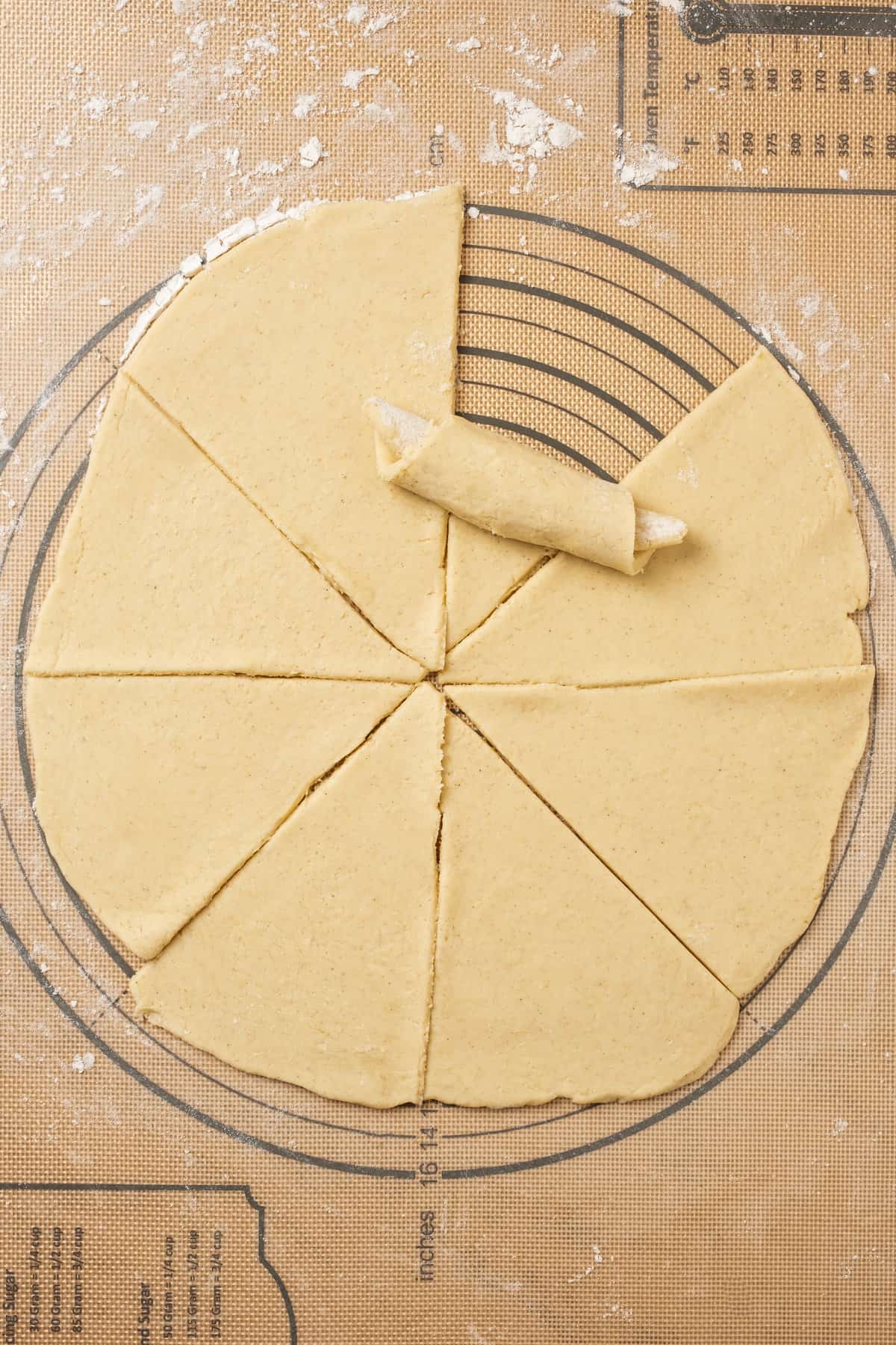 One of eight dough triangles is rolled into a crescent shape on a floured surface.