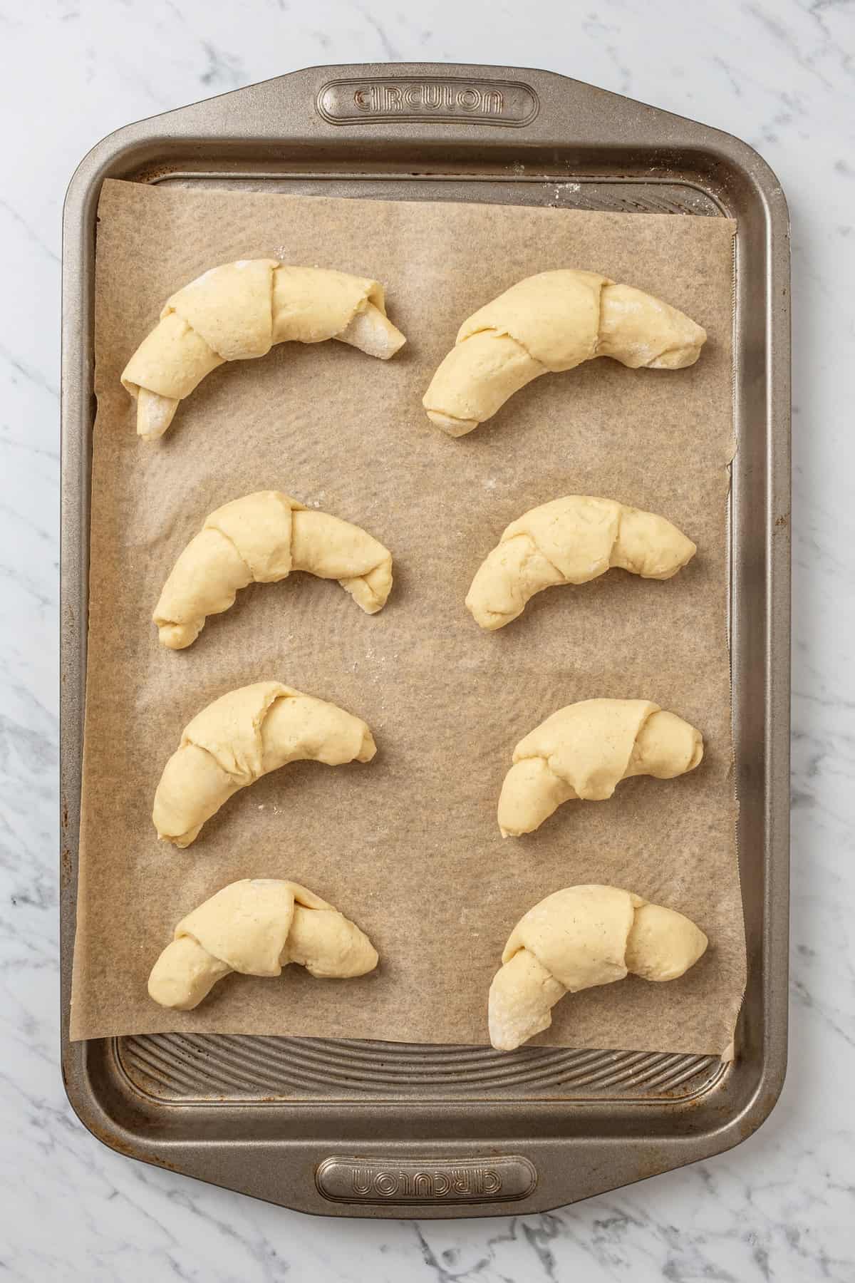 Unbaked gluten free crescent rolls lined up on a parchment-lined baking sheet.