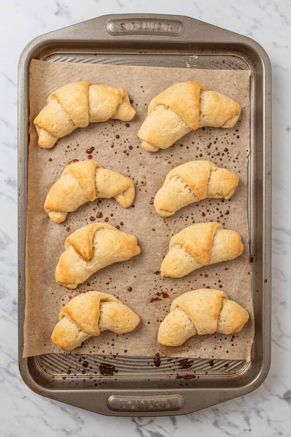 Baked gluten free crescent rolls lined up on a parchment-lined baking sheet.